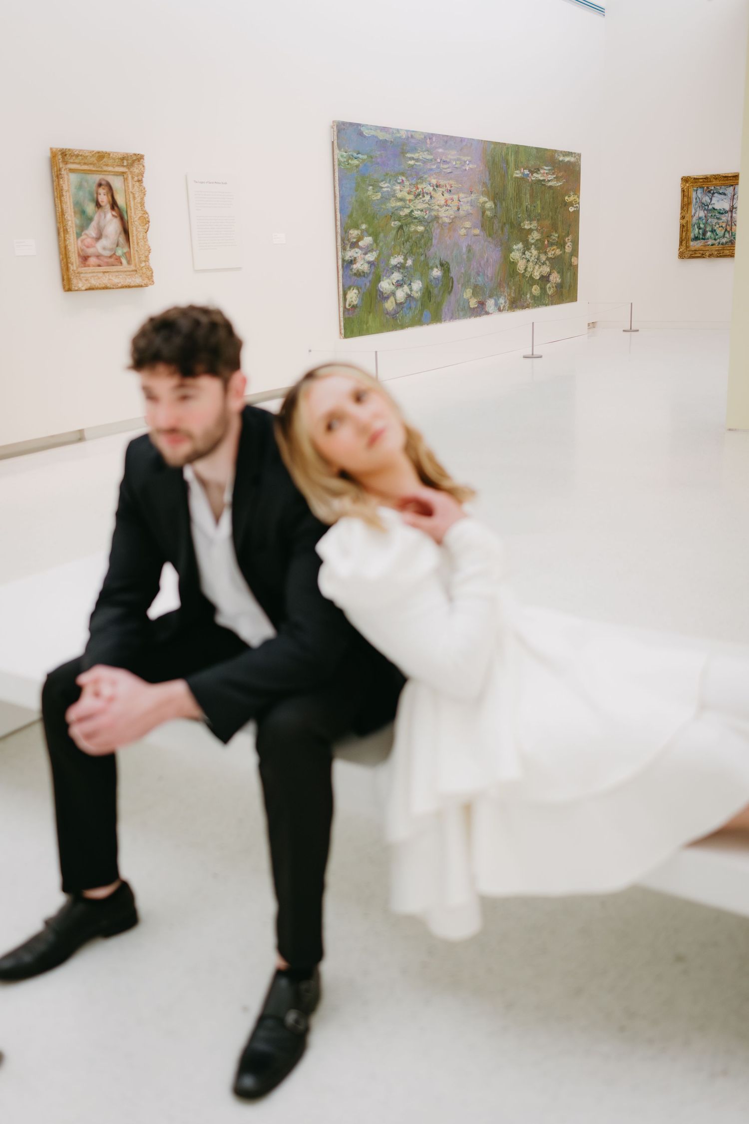 Artistic couple portrait in gallery with paintings displayed on white walls.