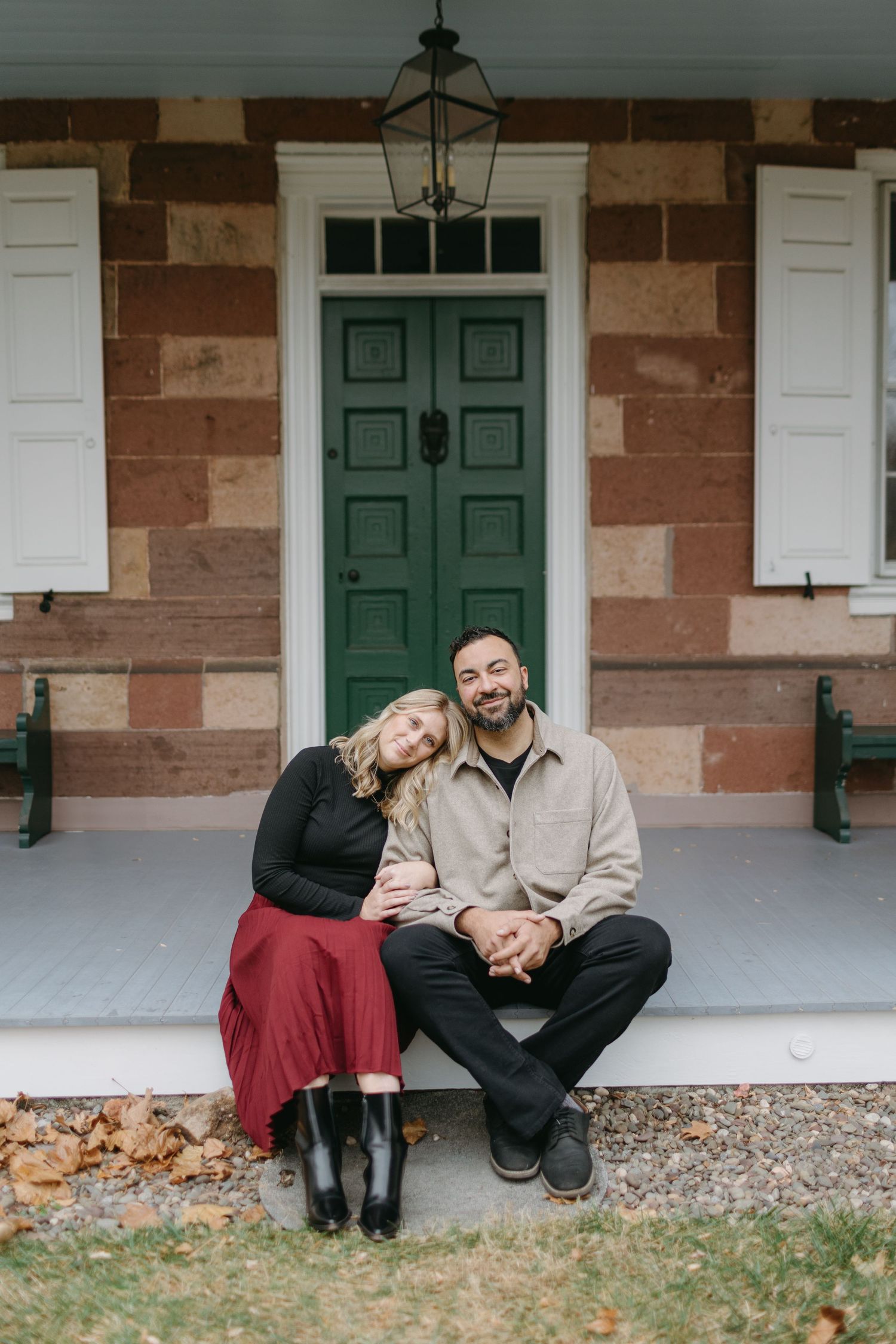A couple sits together on the steps of a historic building with a green door.