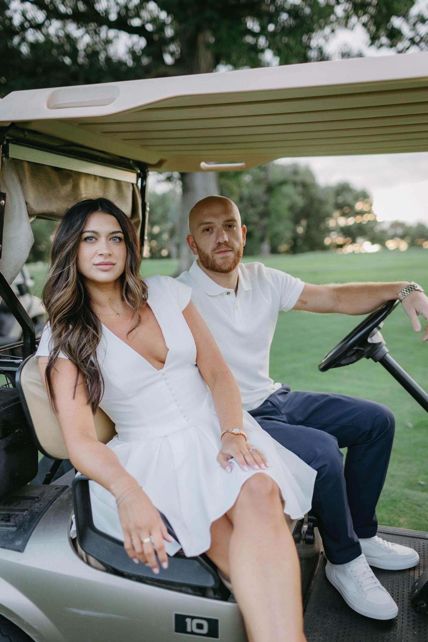 Couple sitting together in golf cart on course during engagement photoshoot.