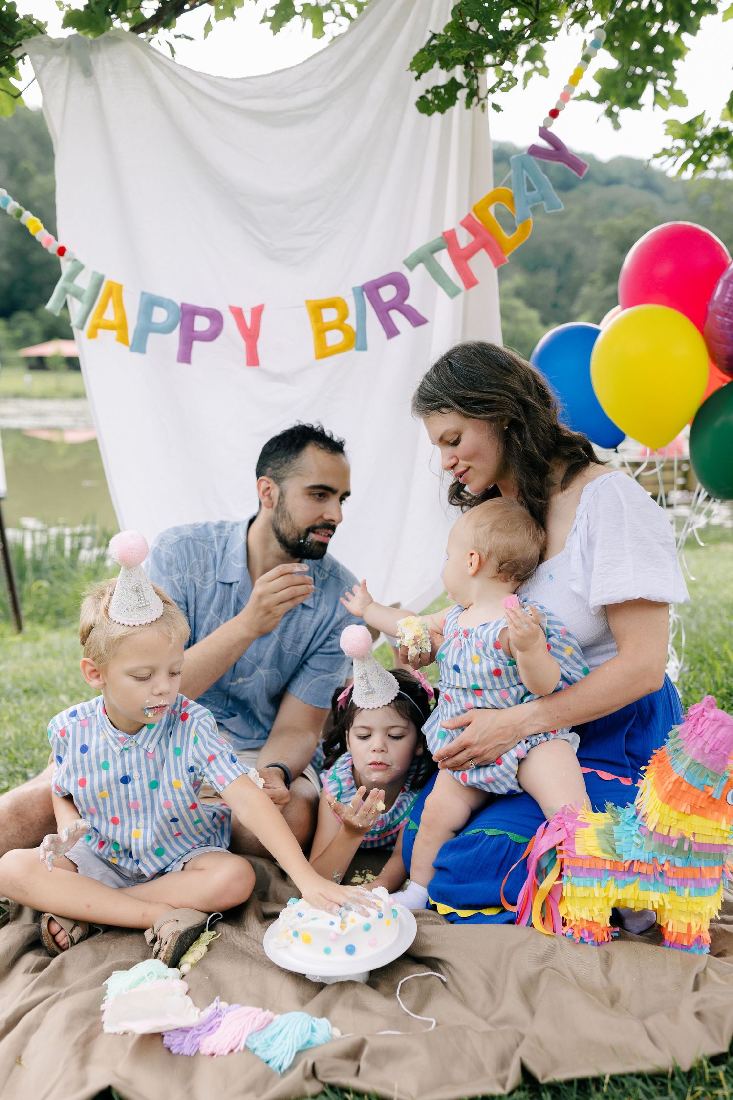 Colorful outdoor birthday party scene with hanging decorations and balloons against a white backdrop.