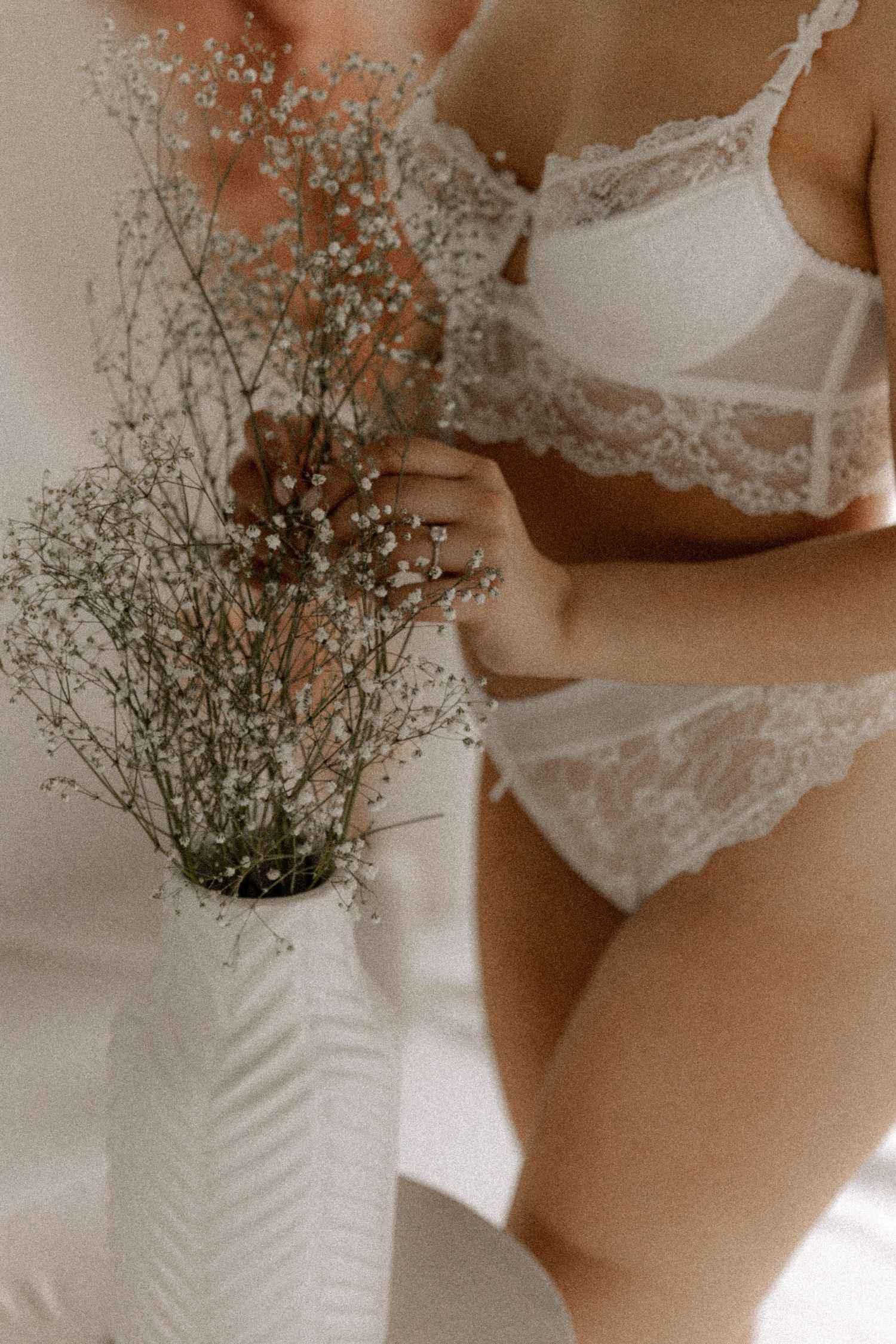 Artistic close-up of white lace lingerie with delicate dried flowers in a white vase.