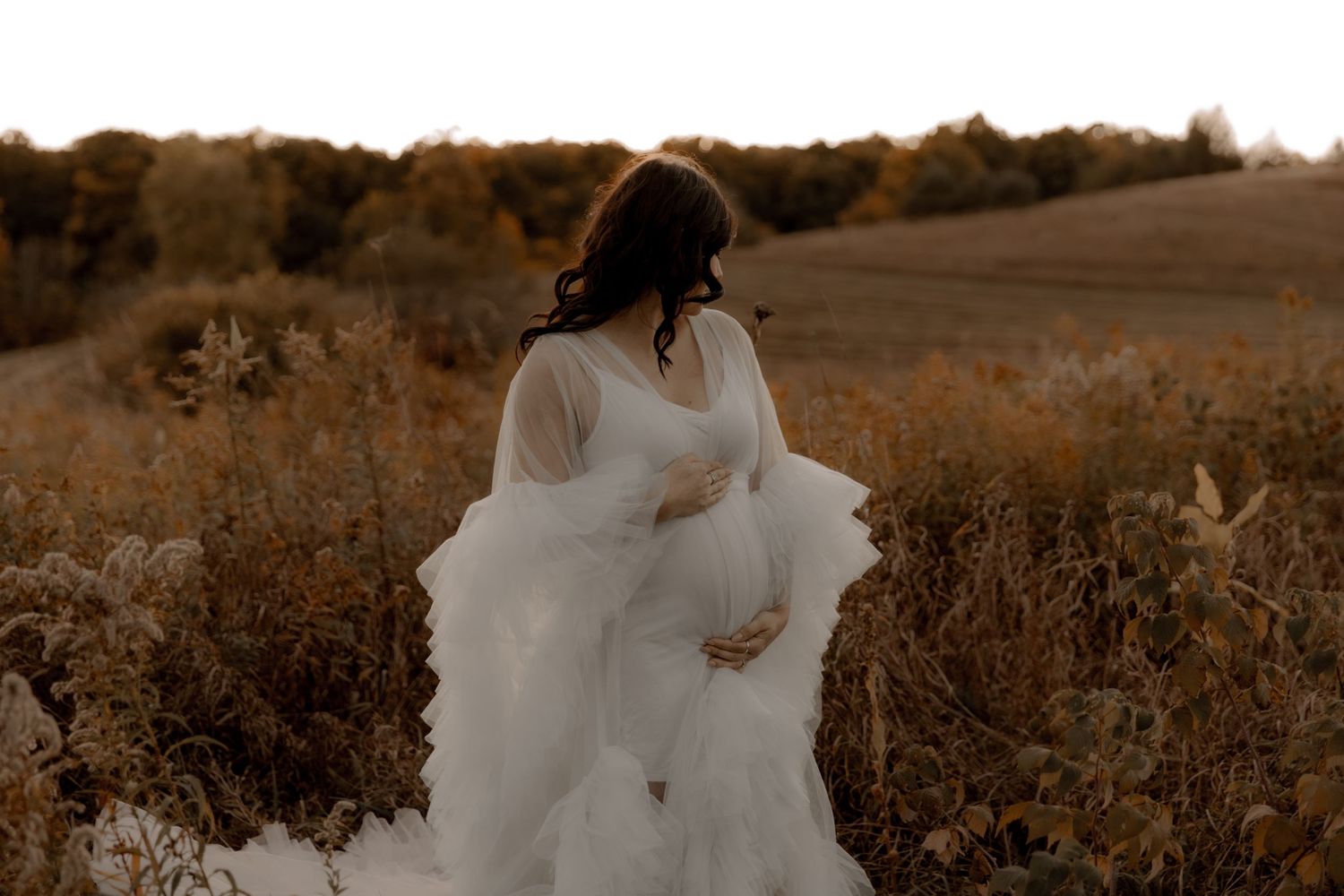 A dreamy maternity photo in warm autumn tones featuring an ethereal white dress.