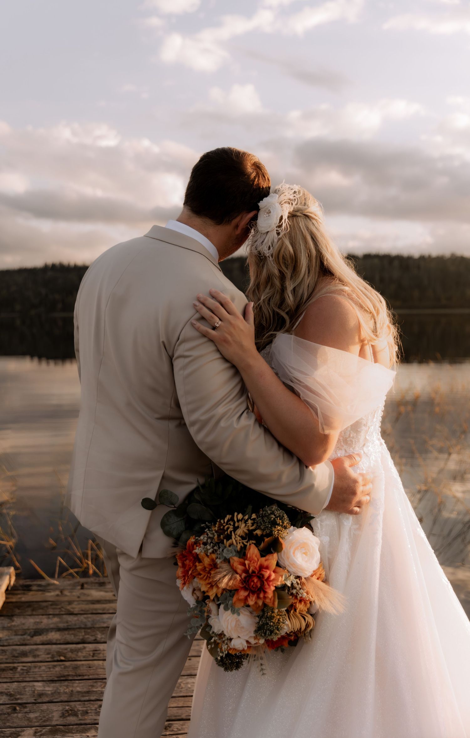 Bride and groom sharing a romantic kiss on a dock by a lake, bride holding autumn bouquet.