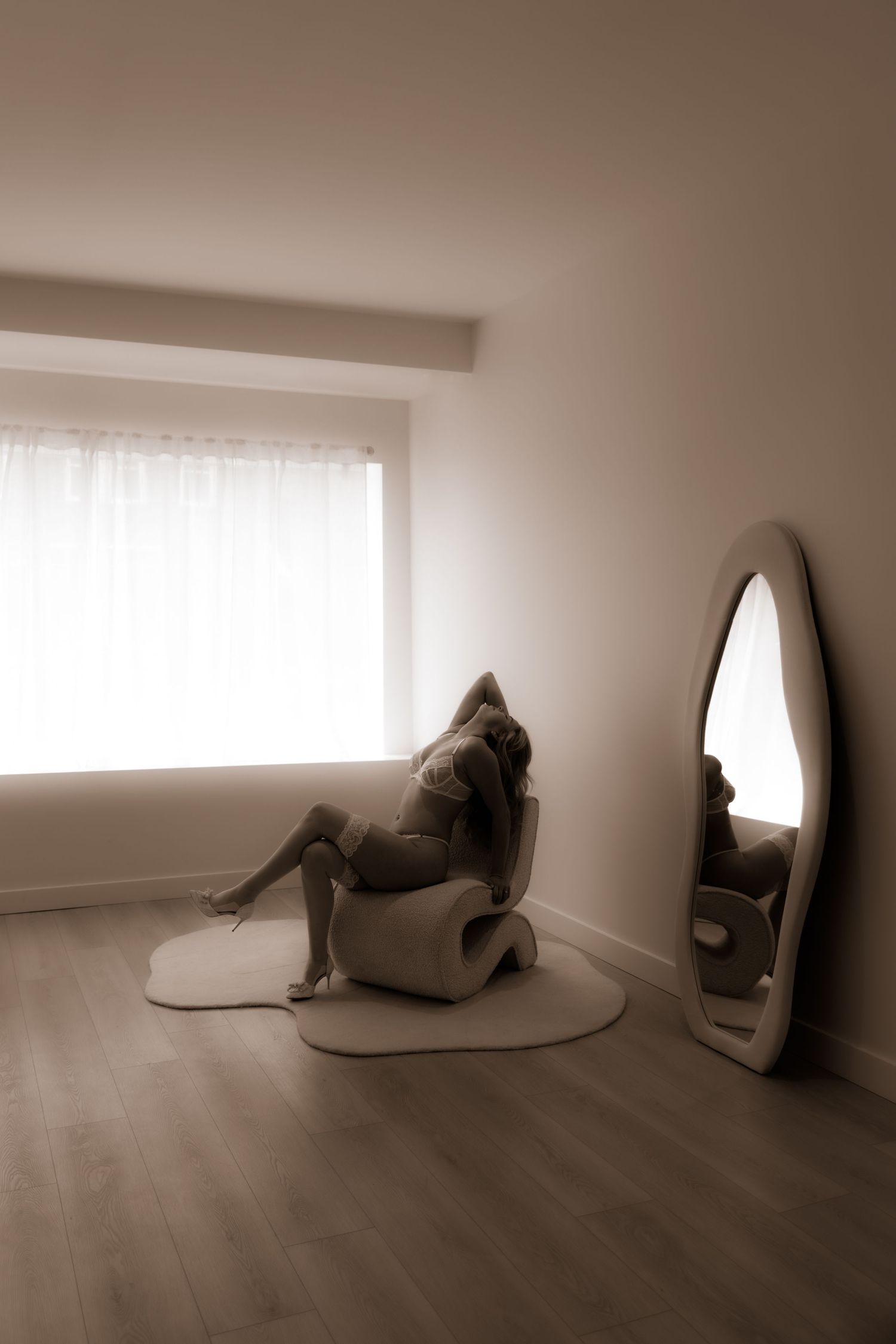 Artistic sepia photograph of an interior scene with mirror and curved furniture elements.