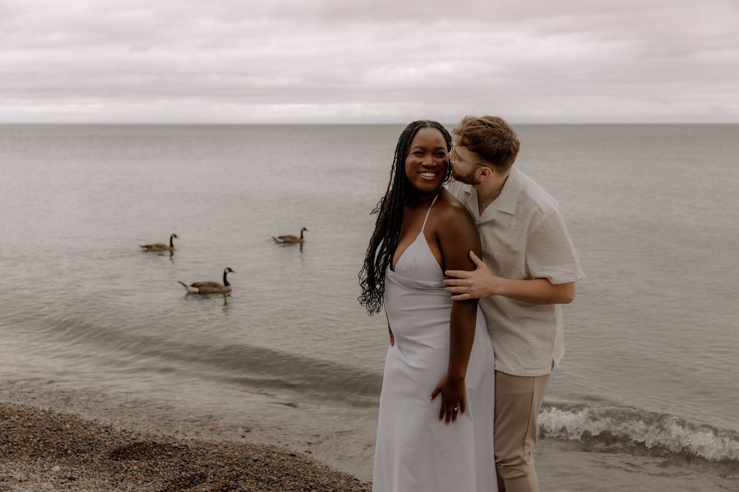 Couple embraces by waterfront as three ducks swim peacefully in background.