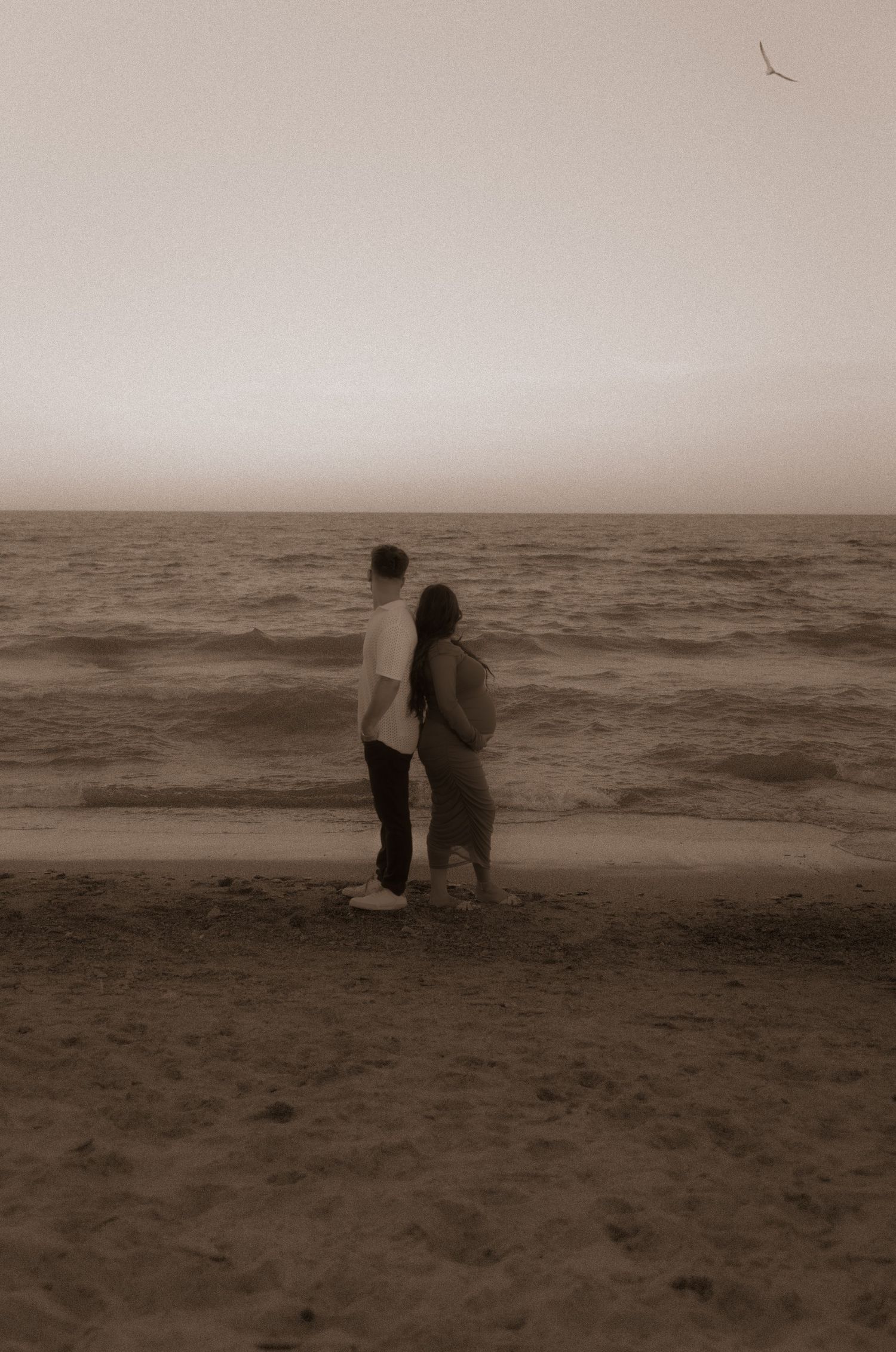 Sepia-toned image of couple standing together on misty beach shoreline.