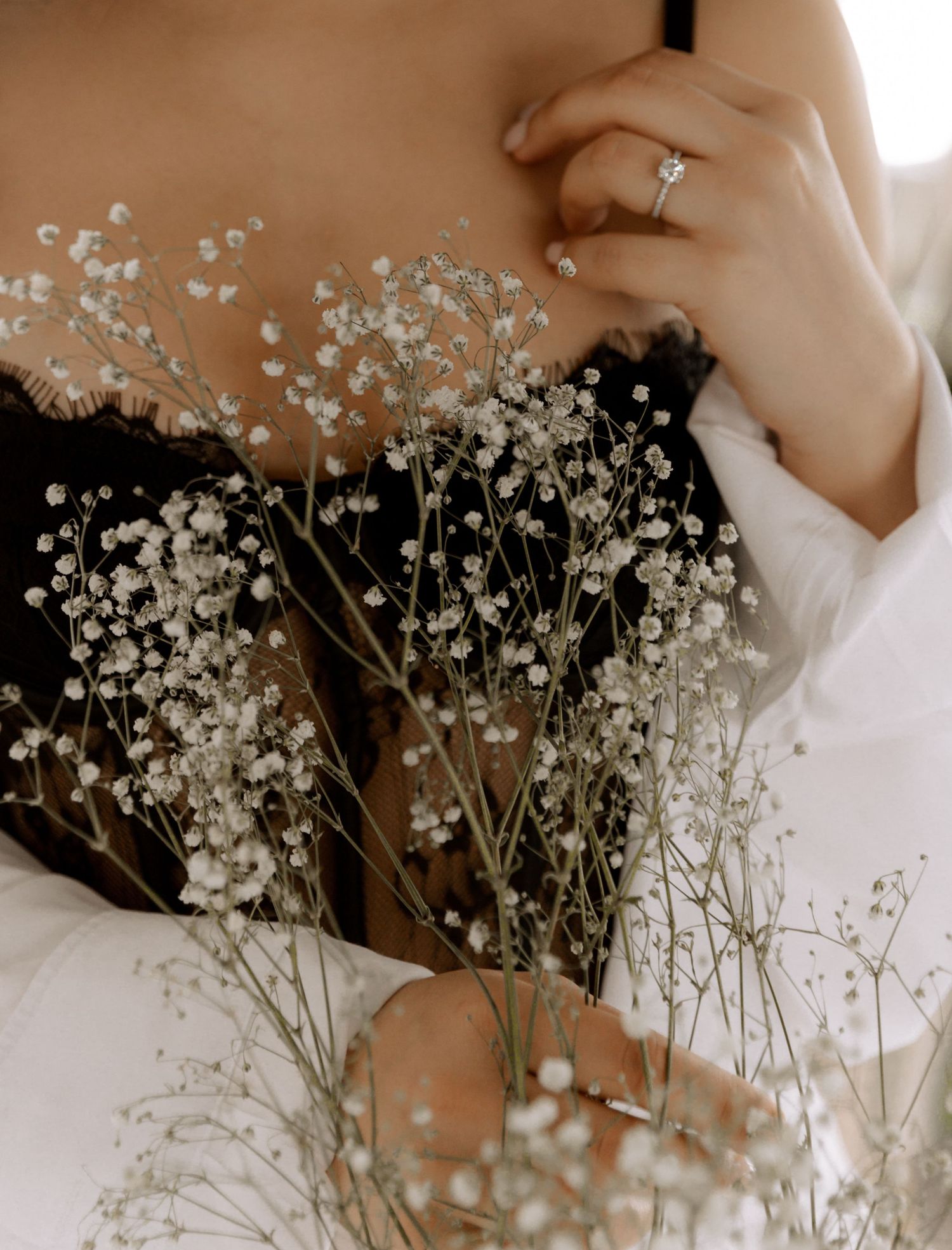 Close-up of hands holding baby's breath flowers with engagement ring detail.
