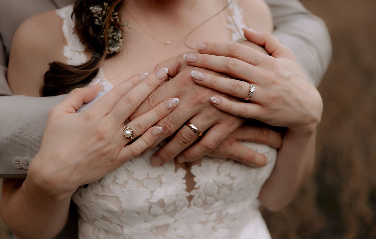 Bride and groom hands with wedding rings resting on white lace wedding dress, close-up detail shot.