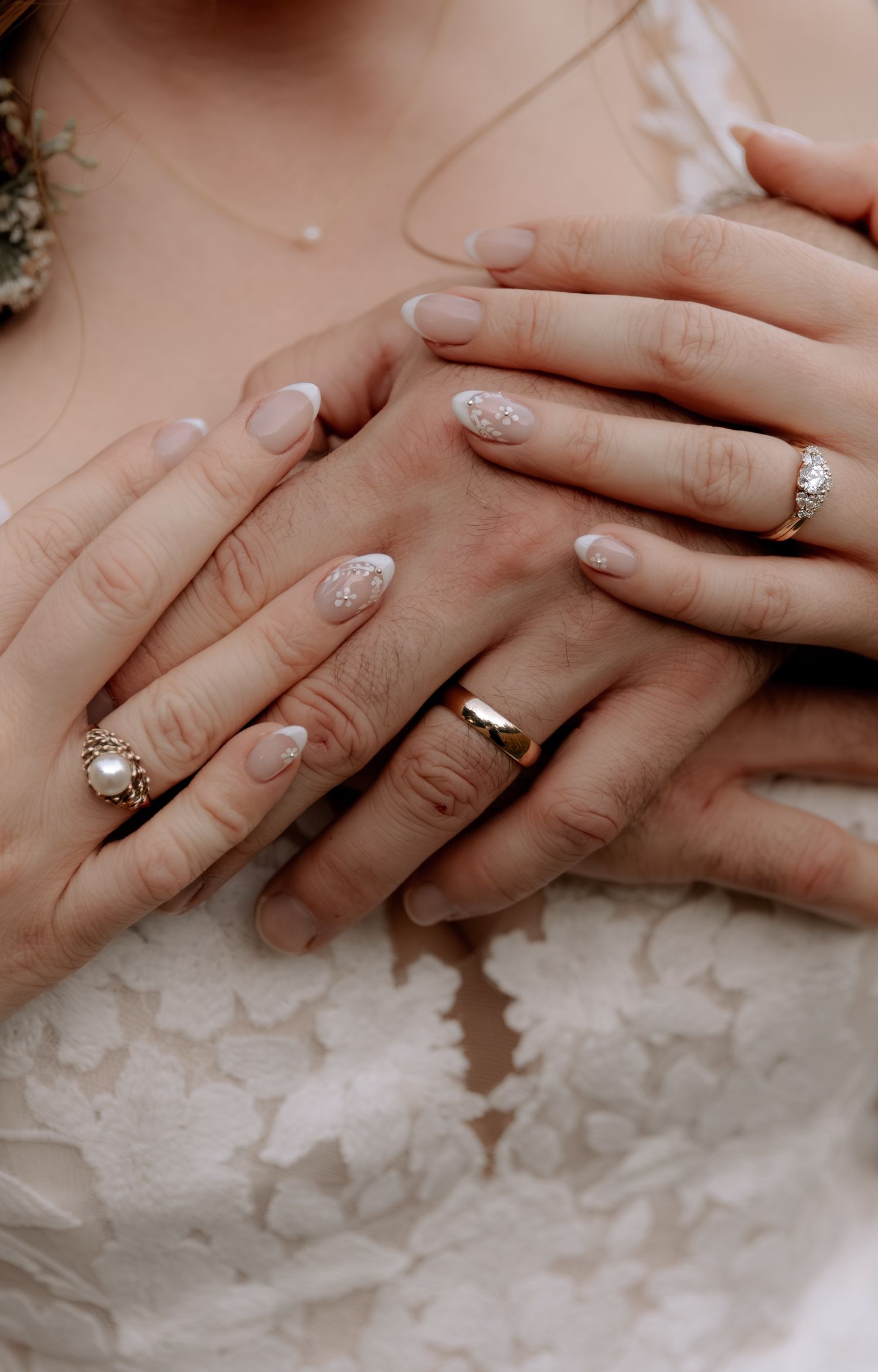 Close-up view of hands with engagement rings resting on white lace fabric showing wedding day details.