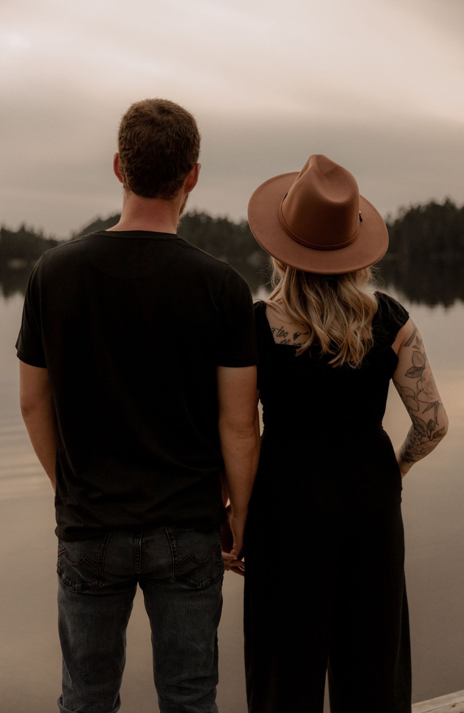 Couple stands together watching sunset by a peaceful lake.