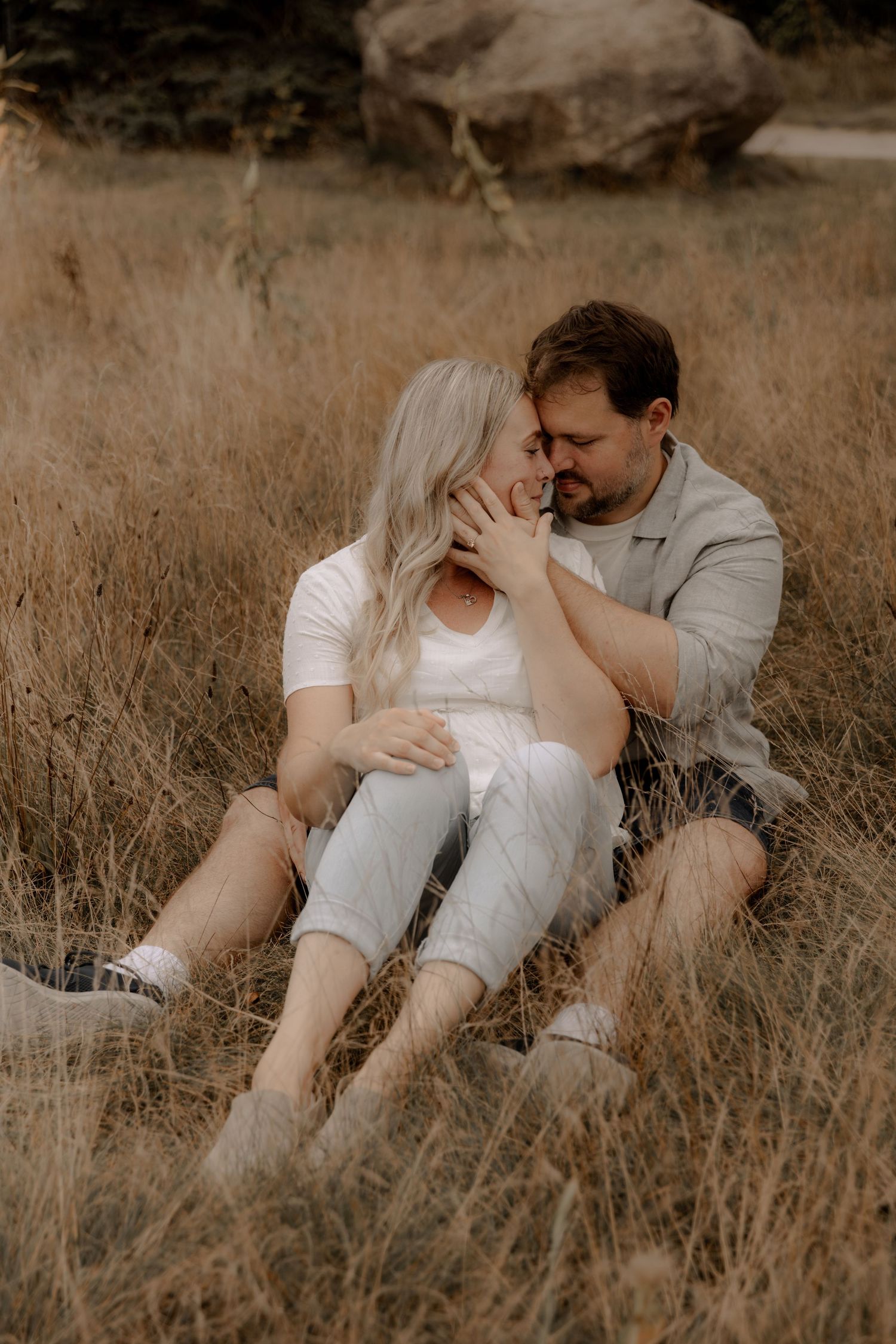Intimate moment shared between couple sitting in rustic field of golden grass.