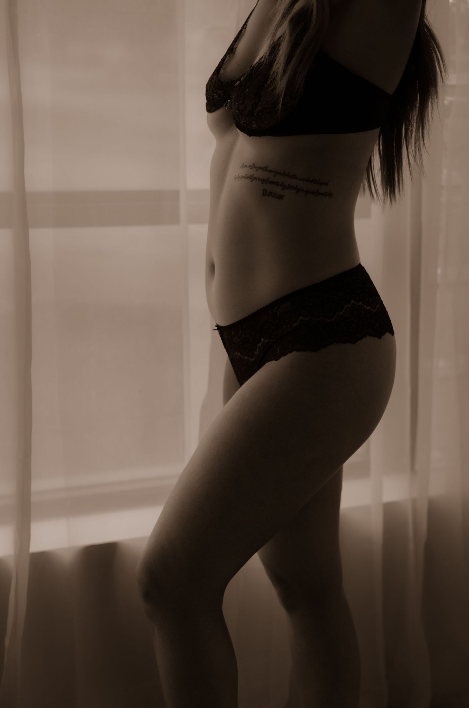 Silhouetted figure in black lingerie against backlit window.