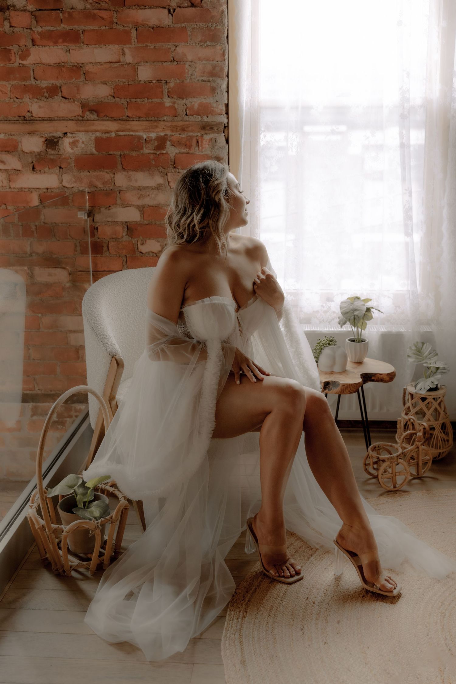Romantic bridal boudoir scene with white flowing dress against exposed brick and bohemian decor.