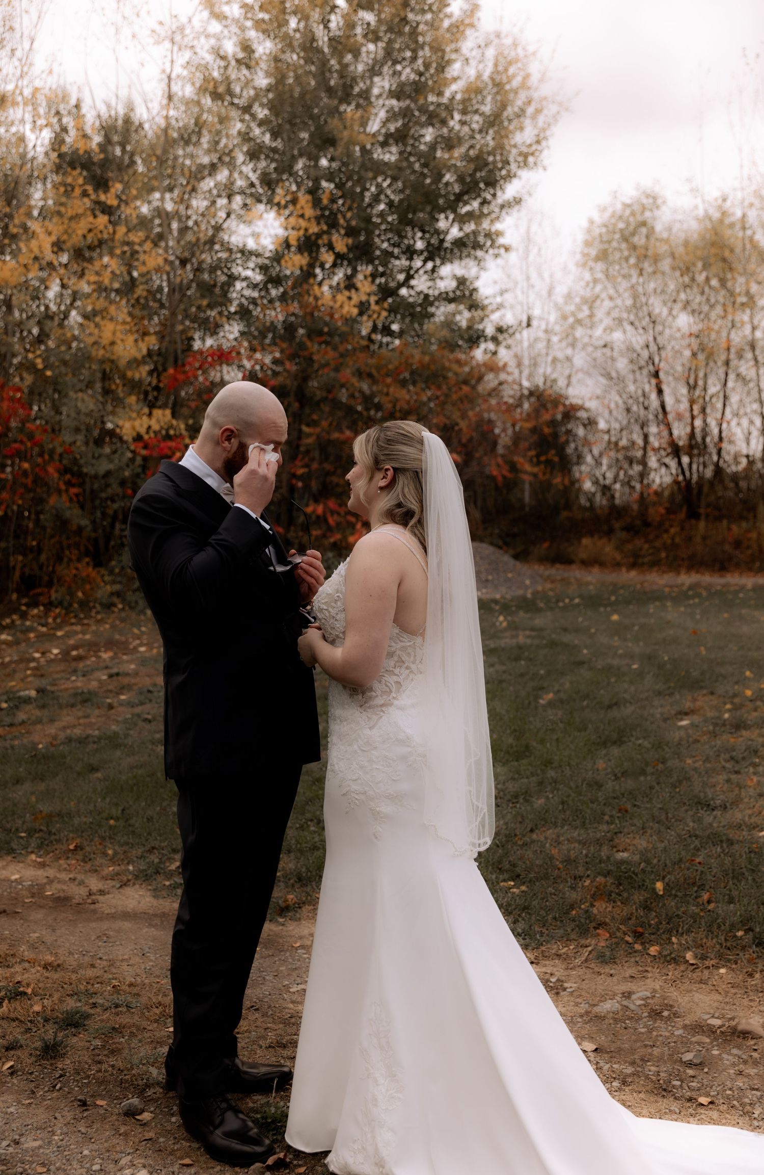 A couple shares an intimate moment during their autumn wedding ceremony on a dirt path surrounded by fall foliage.