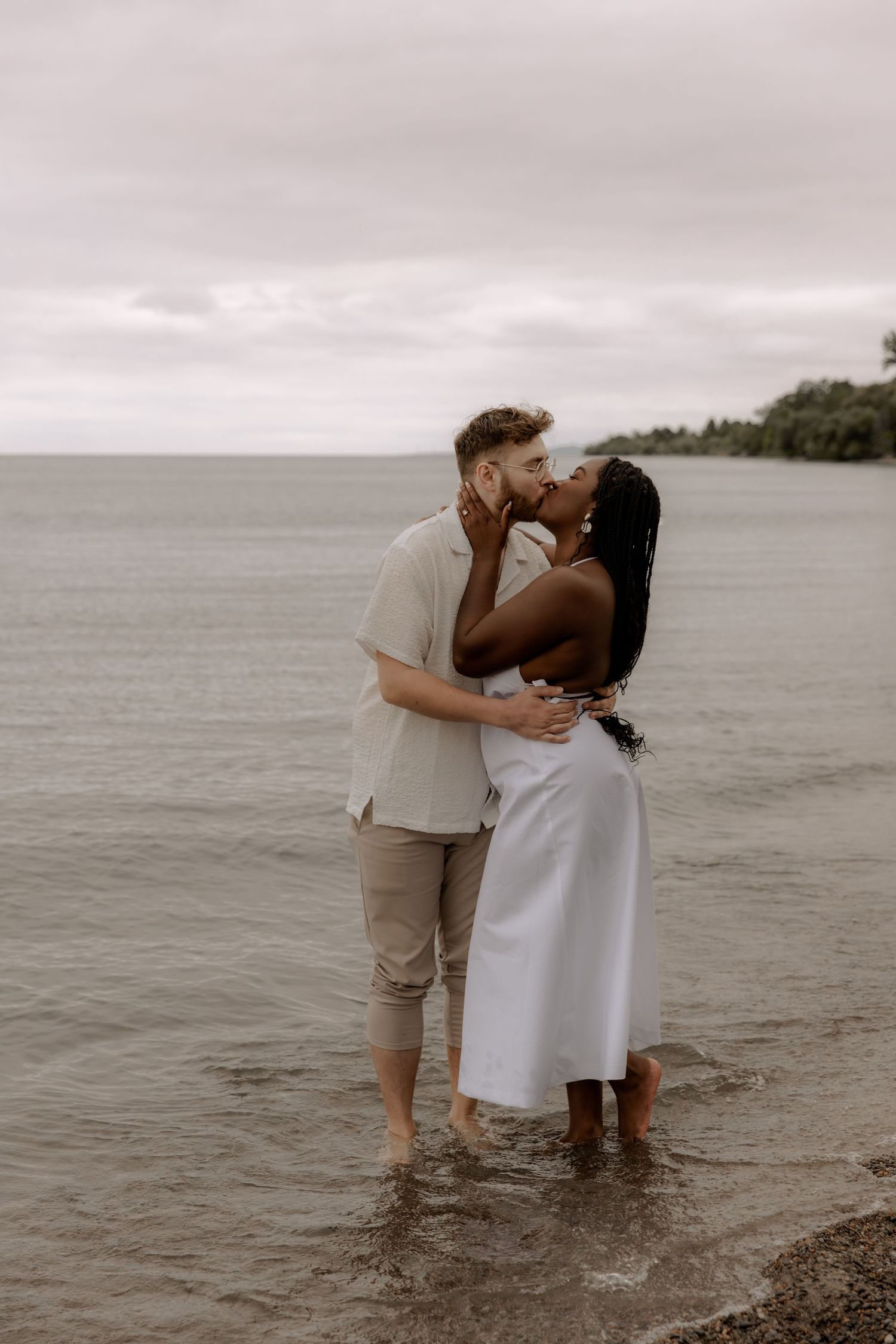 A couple embraces while standing in shallow water at the beach.