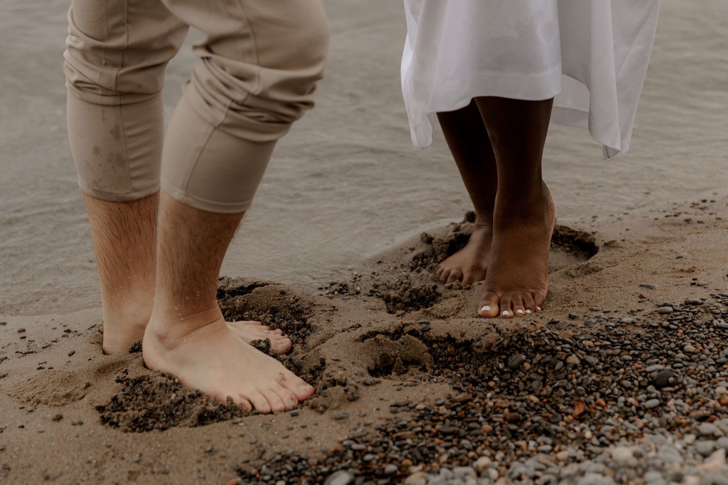 Bare feet of two people standing in wet sand at the beach edge.