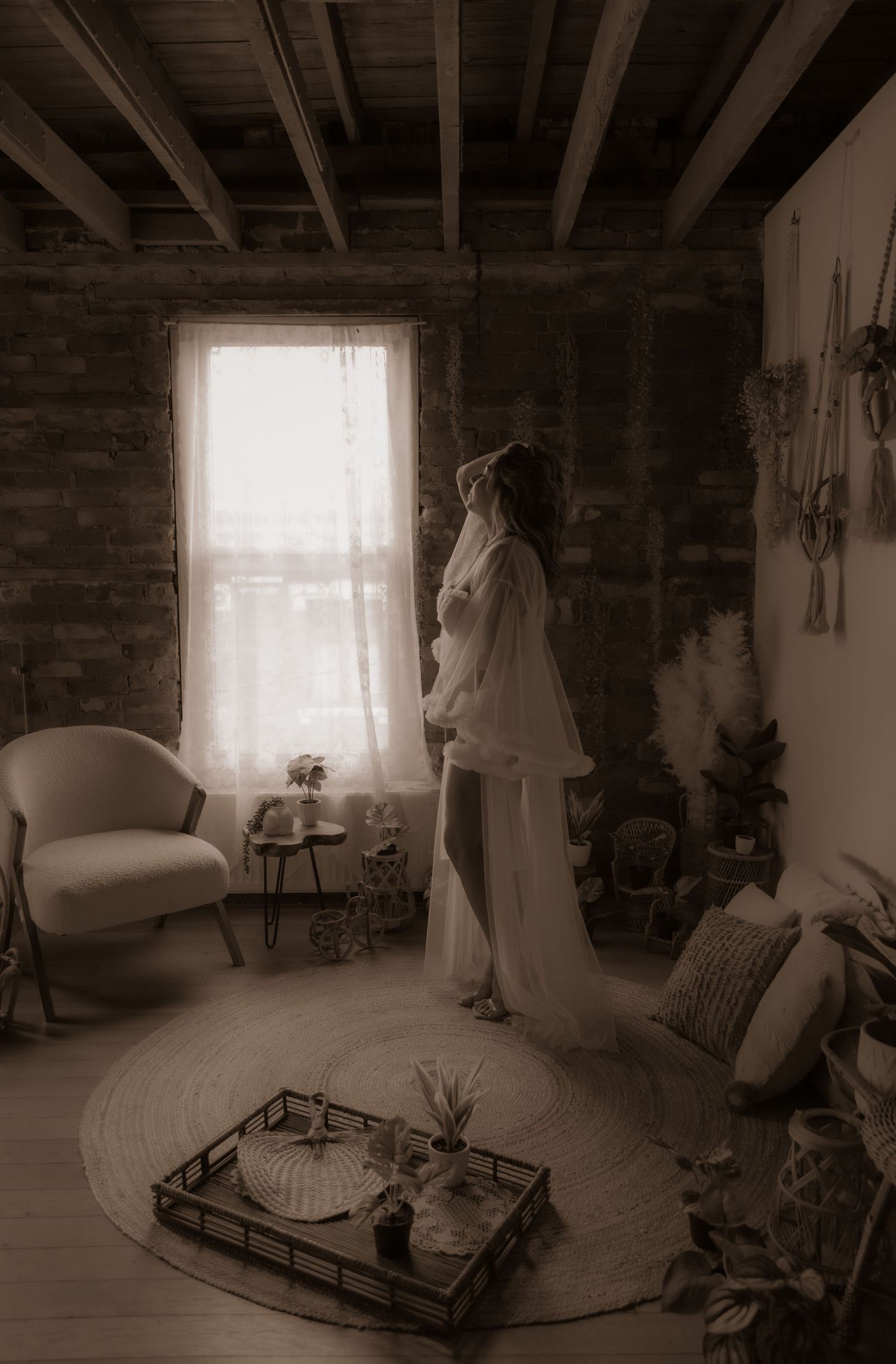 A sepia-toned vintage style photograph of someone in a bridal gown standing by a window in a rustic interior room.