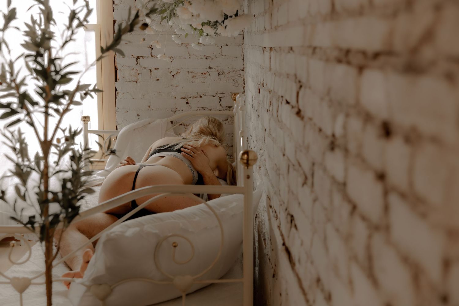 An intimate boudoir photo with an ethereal moody atmosphere against white brick walls.