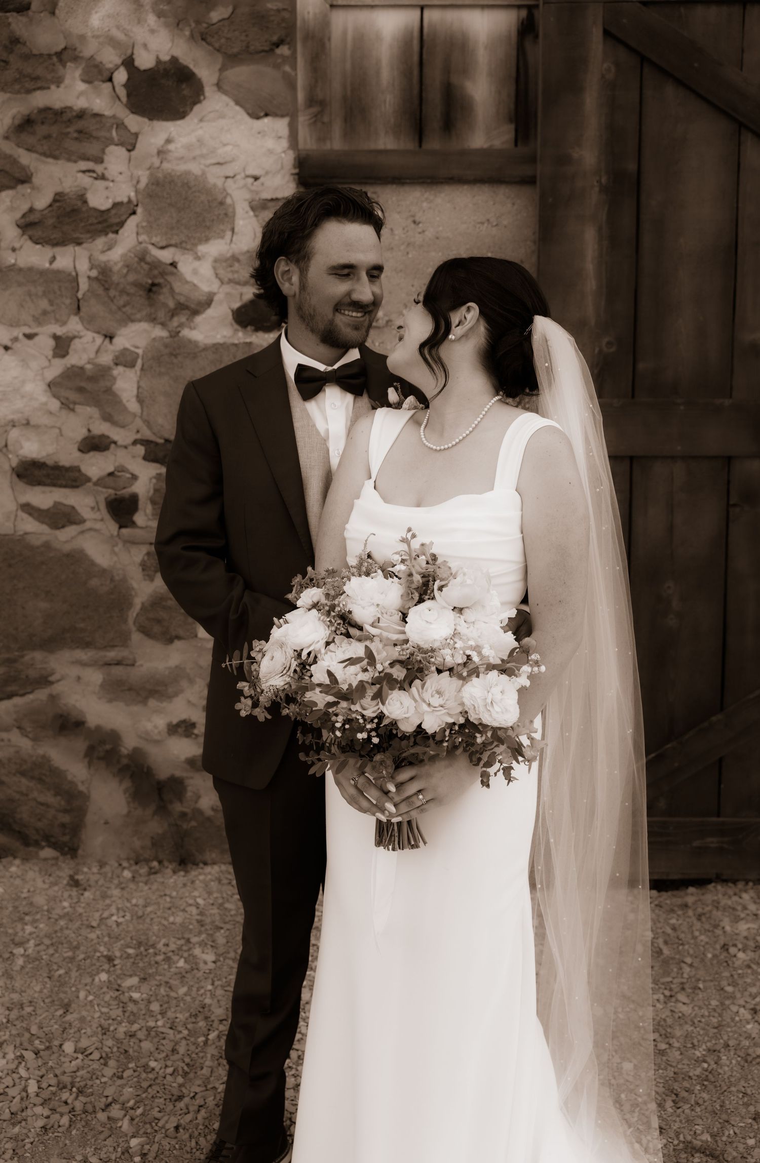 A romantic sepia-toned wedding photo series showing a couple in formal attire against a rustic stone wall.