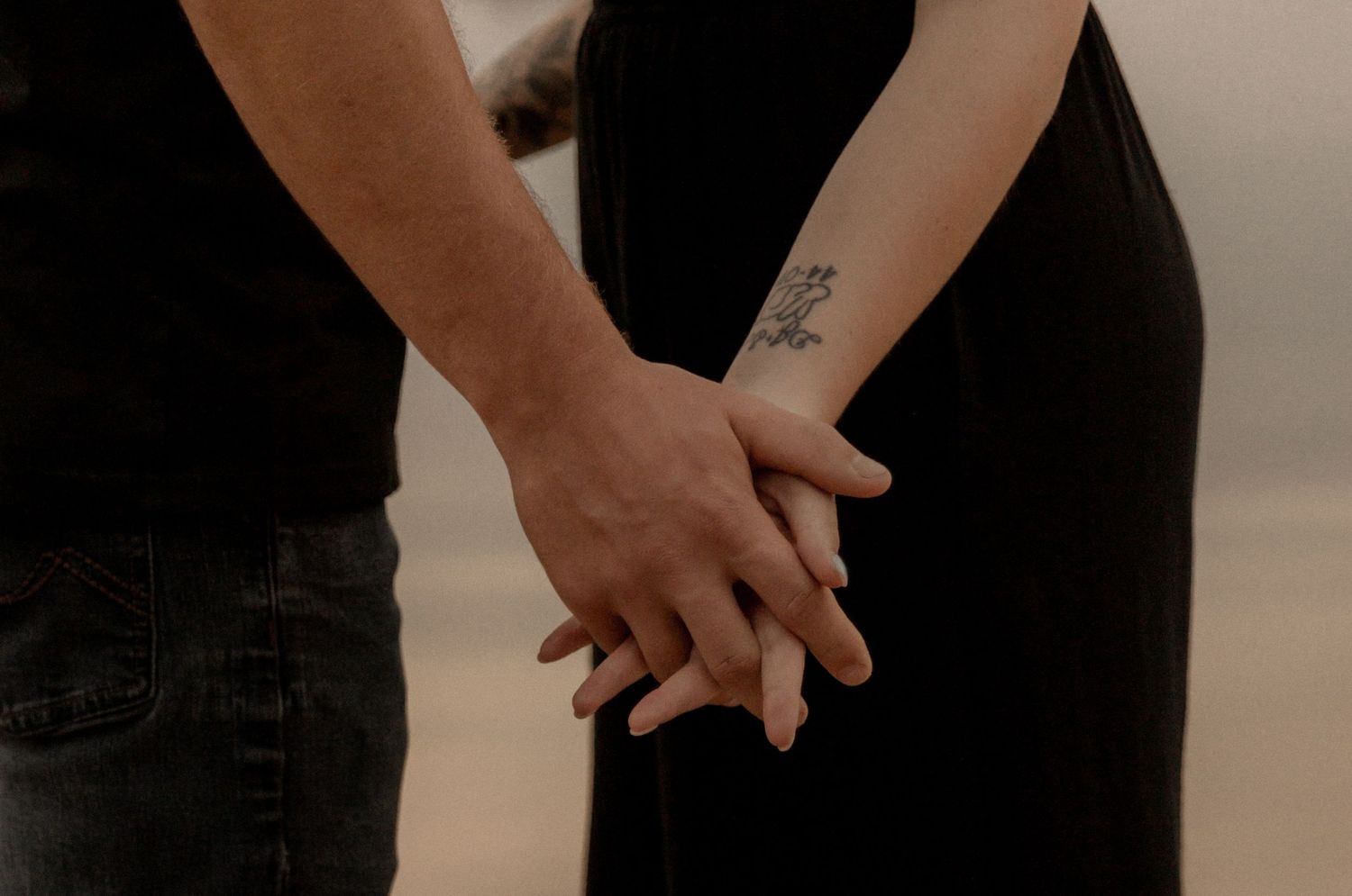 Close-up of two people holding hands against sunset lake backdrop.