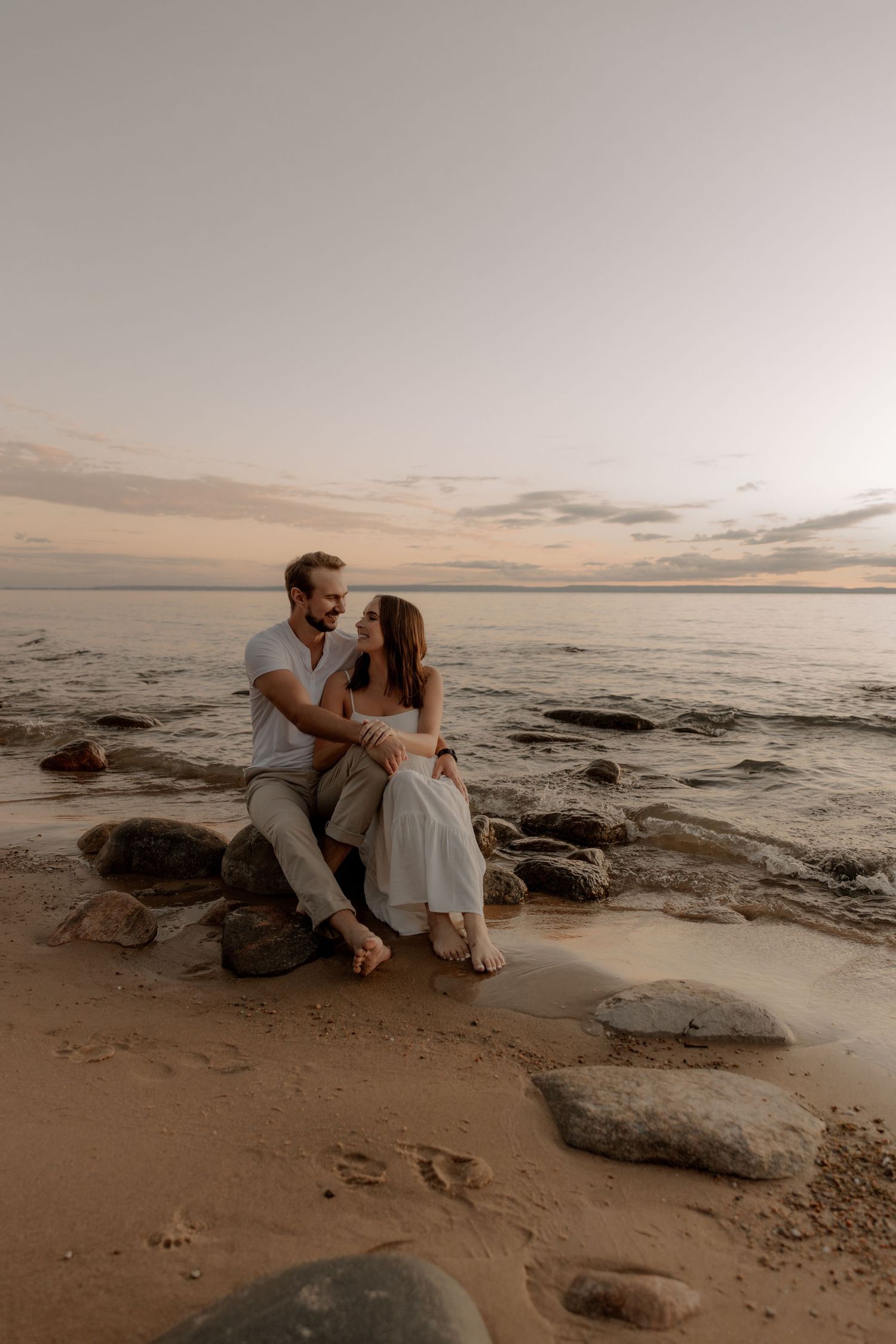 Intimate beachside portrait of couple sitting on coastal rocks during sunset.