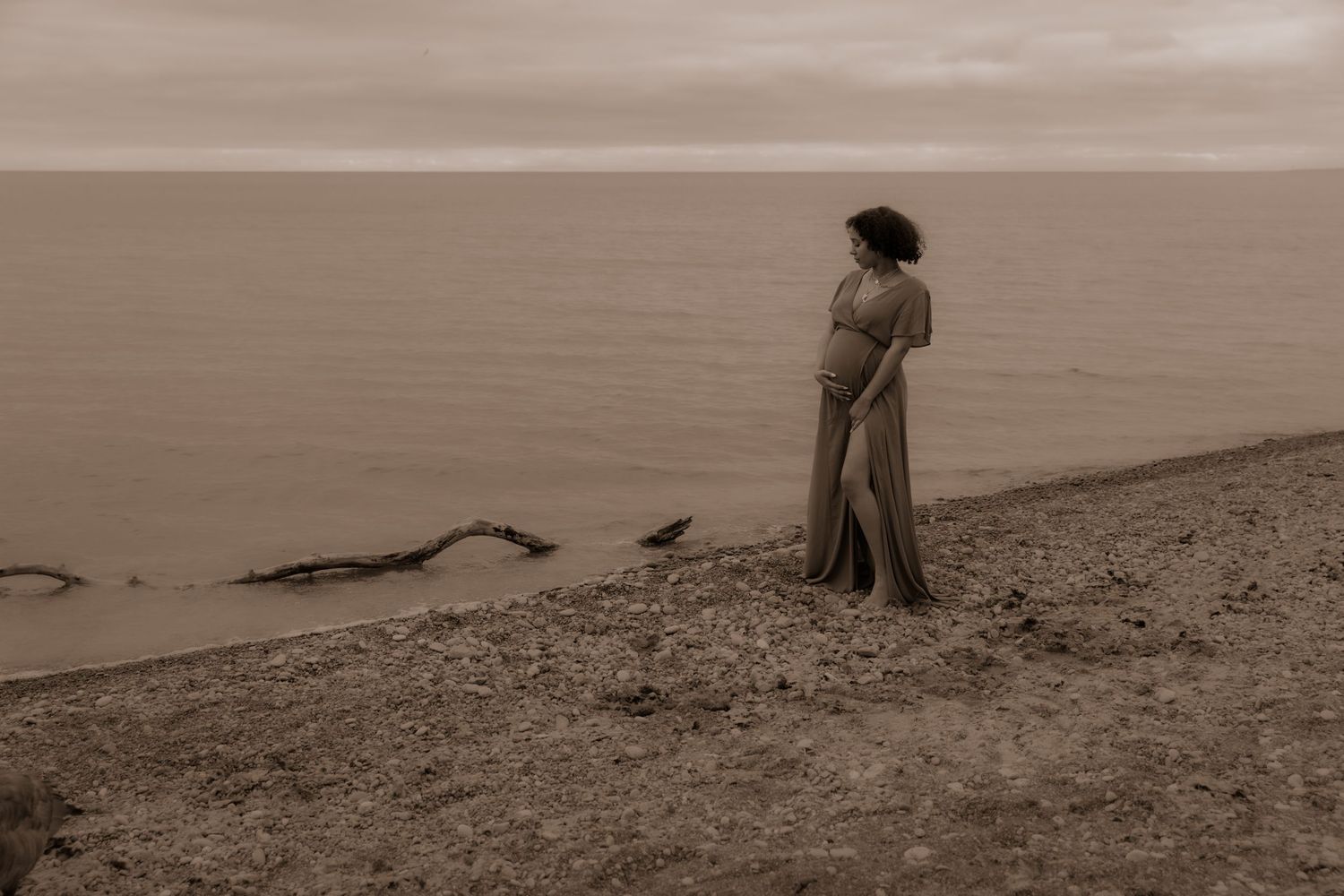 A silhouette stands contemplatively on a coastal cliff in sepia tones.