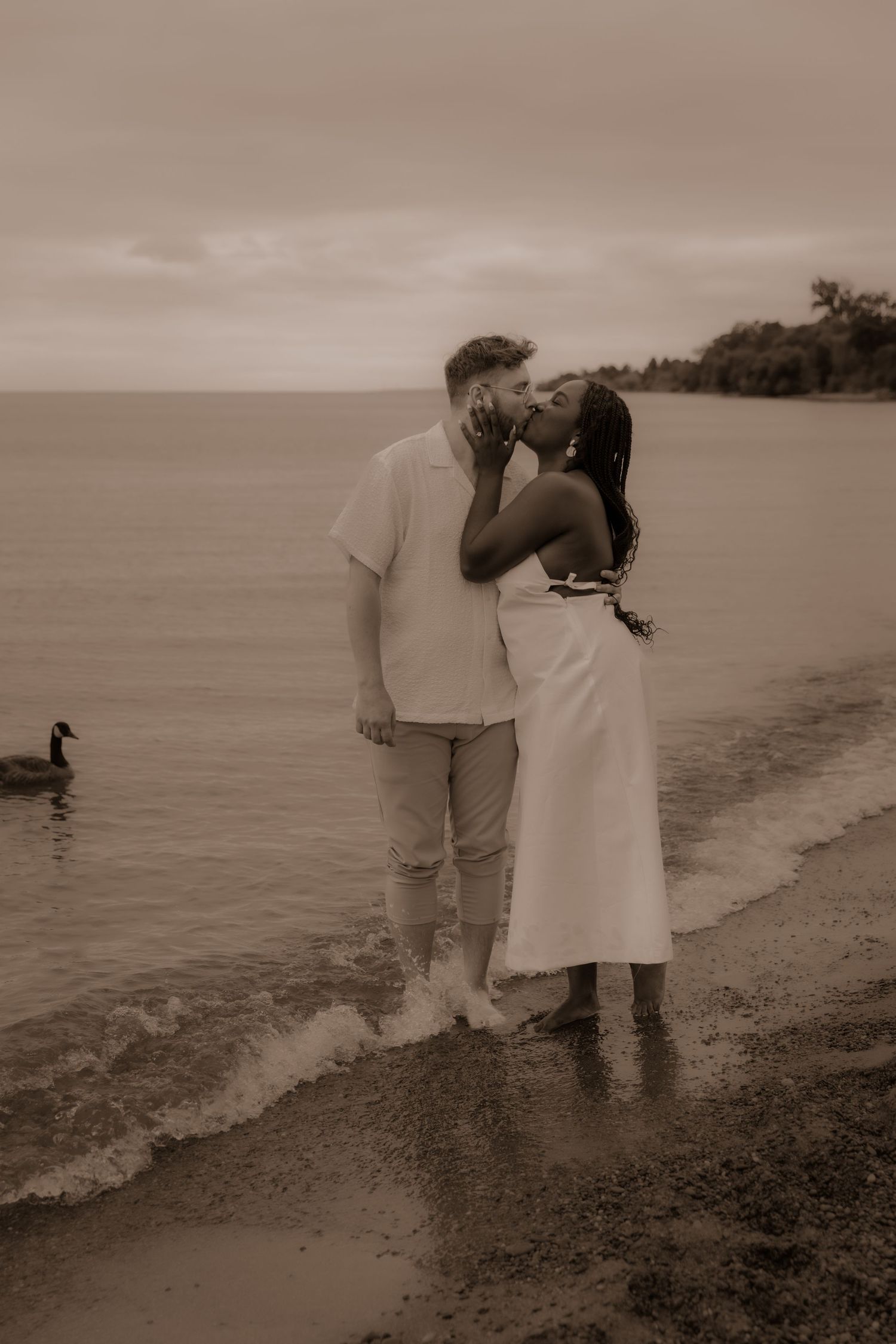 A couple shares a tender moment on the beach in sepia tones.