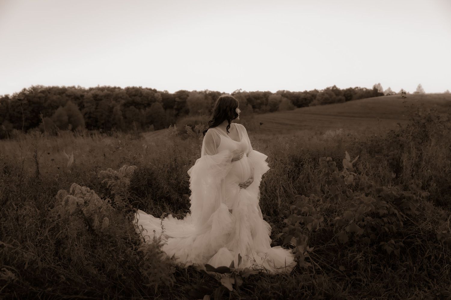 Artistic sepia portrait showing a person in flowing white dress against rolling hills and natural landscape.
