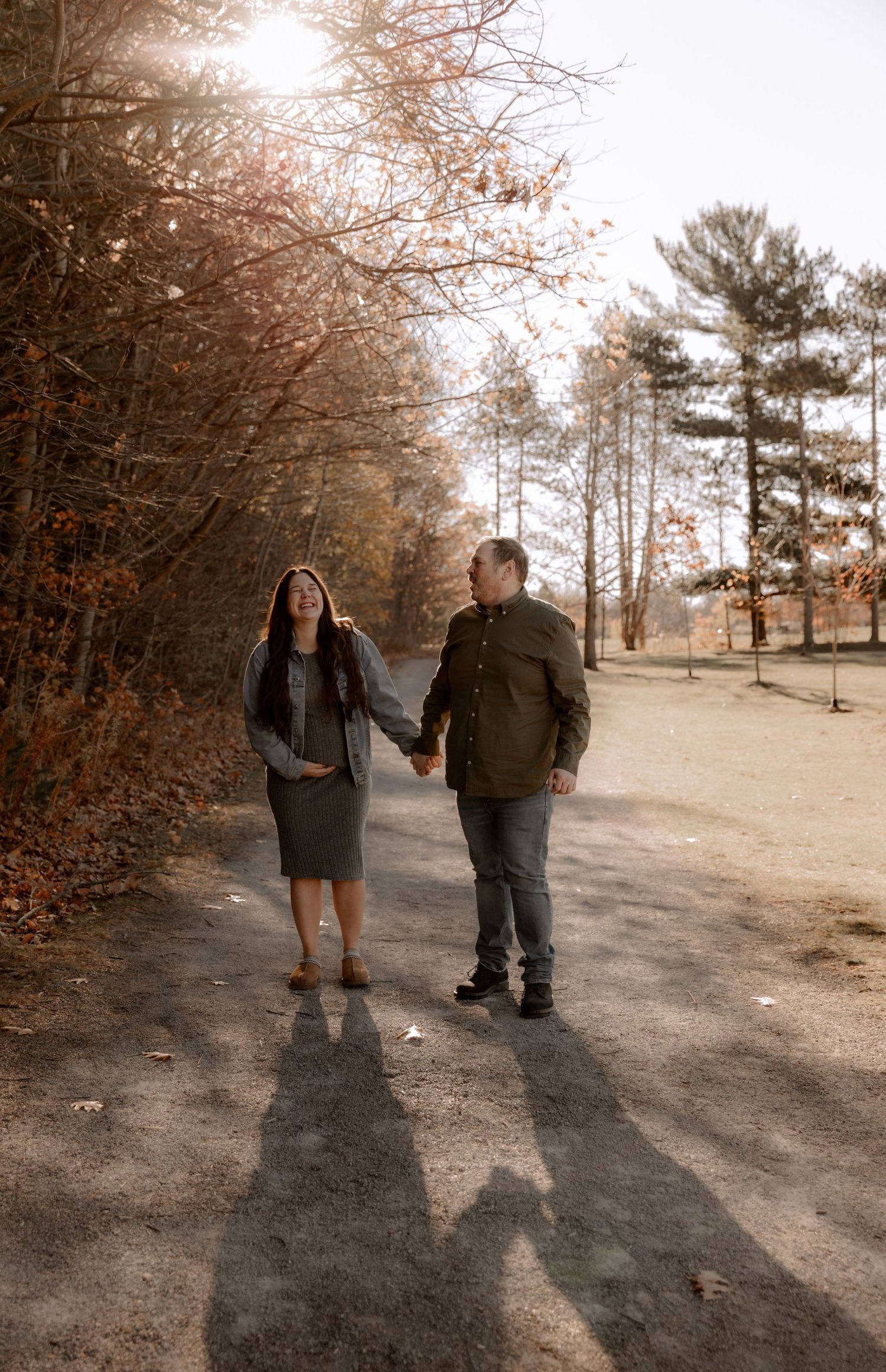 A couple takes a peaceful autumn walk along a tree-lined path holding hands.