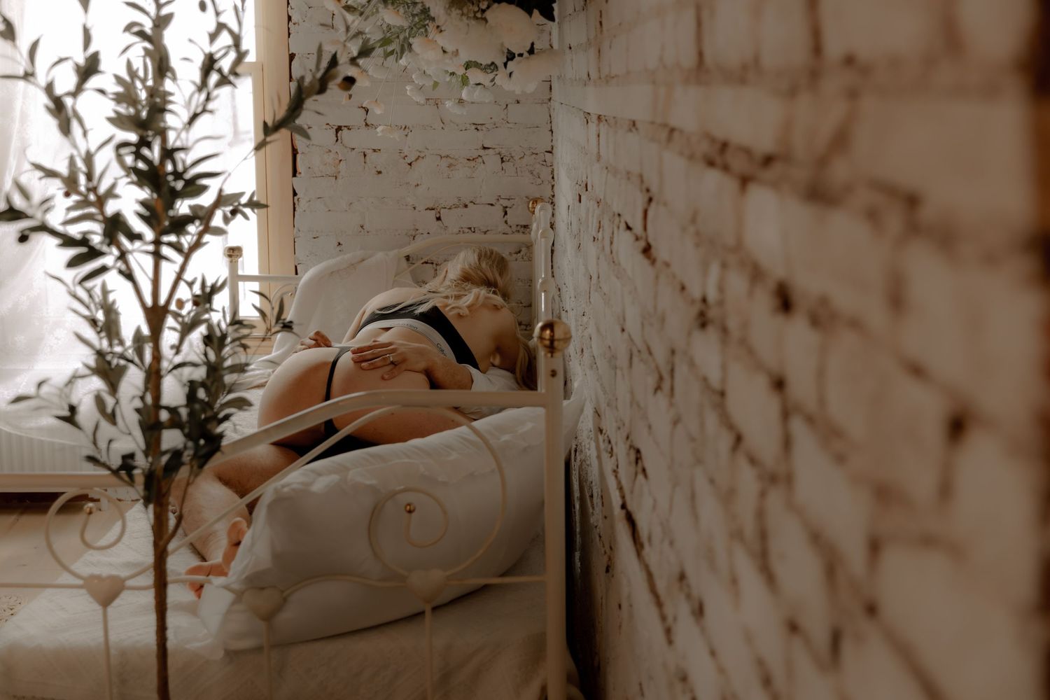 Sepia-toned intimate bedroom scene with white furniture against distressed brick walls.