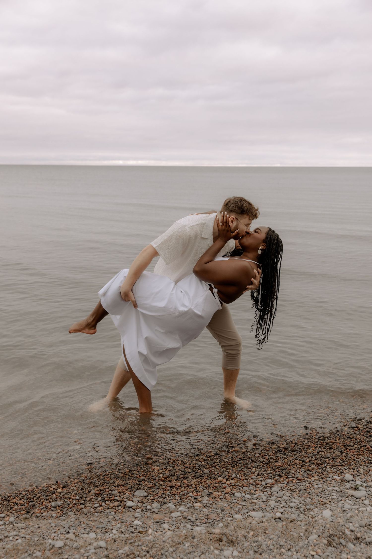 A romantic dip pose on the beach with waves lapping at their feet.
