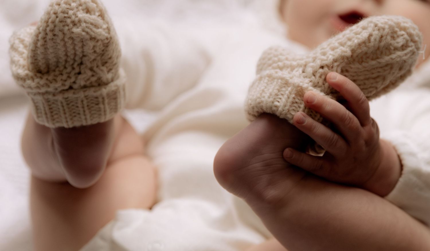 Close-up of a newborn baby wearing knitted booties, with an adult gently holding the infant's tiny feet.