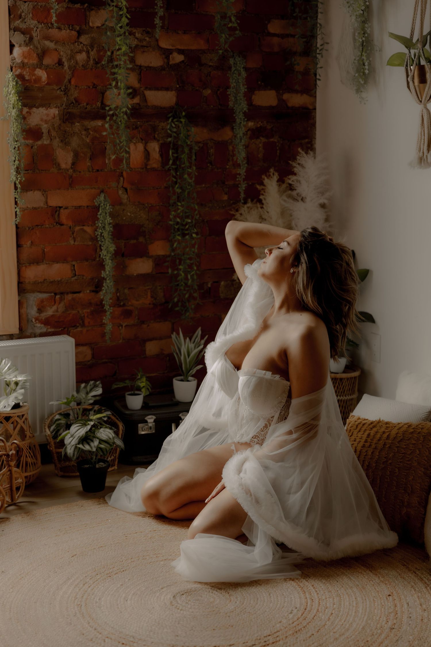 Artistic boudoir photography with flowing white fabric in a plant-filled rustic setting.