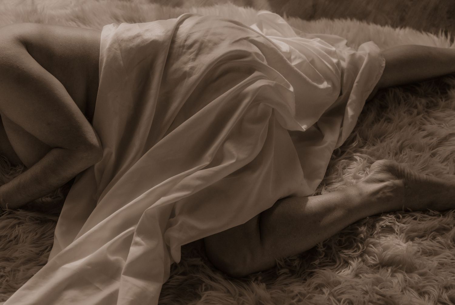 Sepia toned artistic photo of flowing fabric on textured rug.