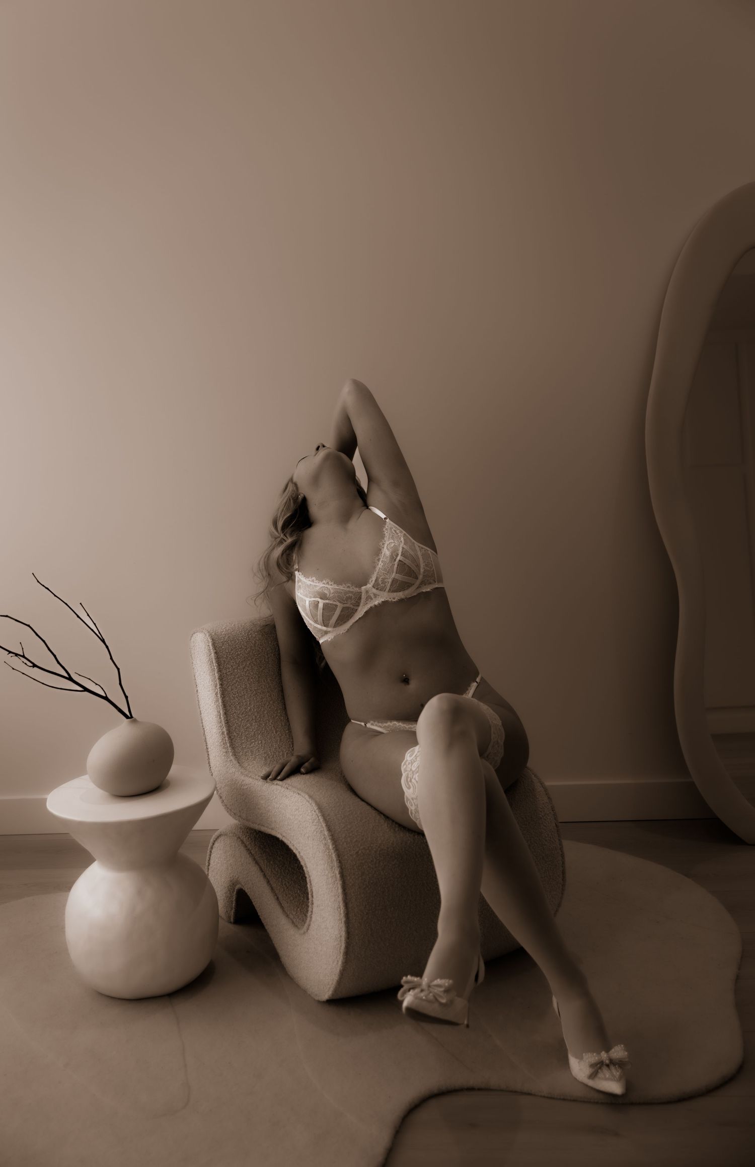 Artistic sepia-toned boudoir photograph with chair and decorative vase.