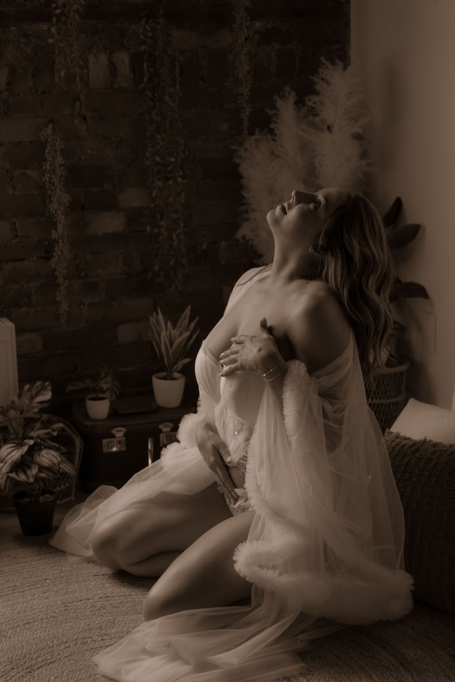 Dramatic sepia portrait featuring soft fabric and natural lighting against textured brick wall.