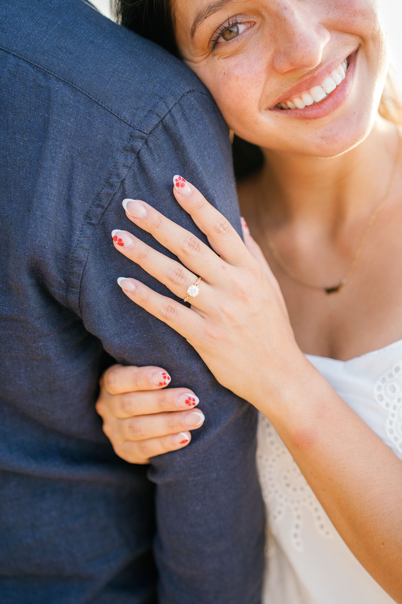 A close-up of hands wearing a sparkling engagement ring against a navy blue shirt and white dress.