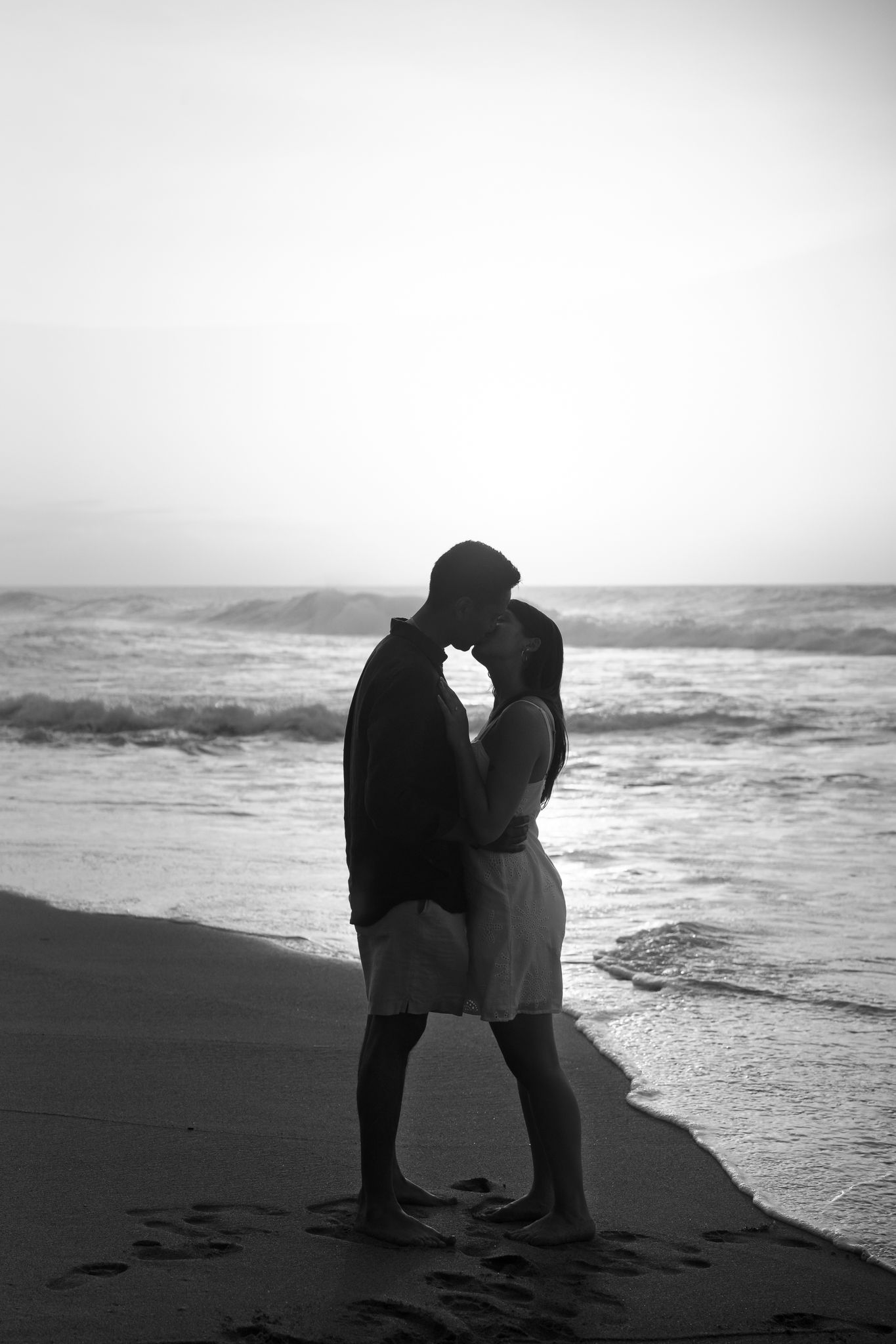 Silhouetted couple sharing an intimate moment on a misty beach at sunset with waves crashing in the background.