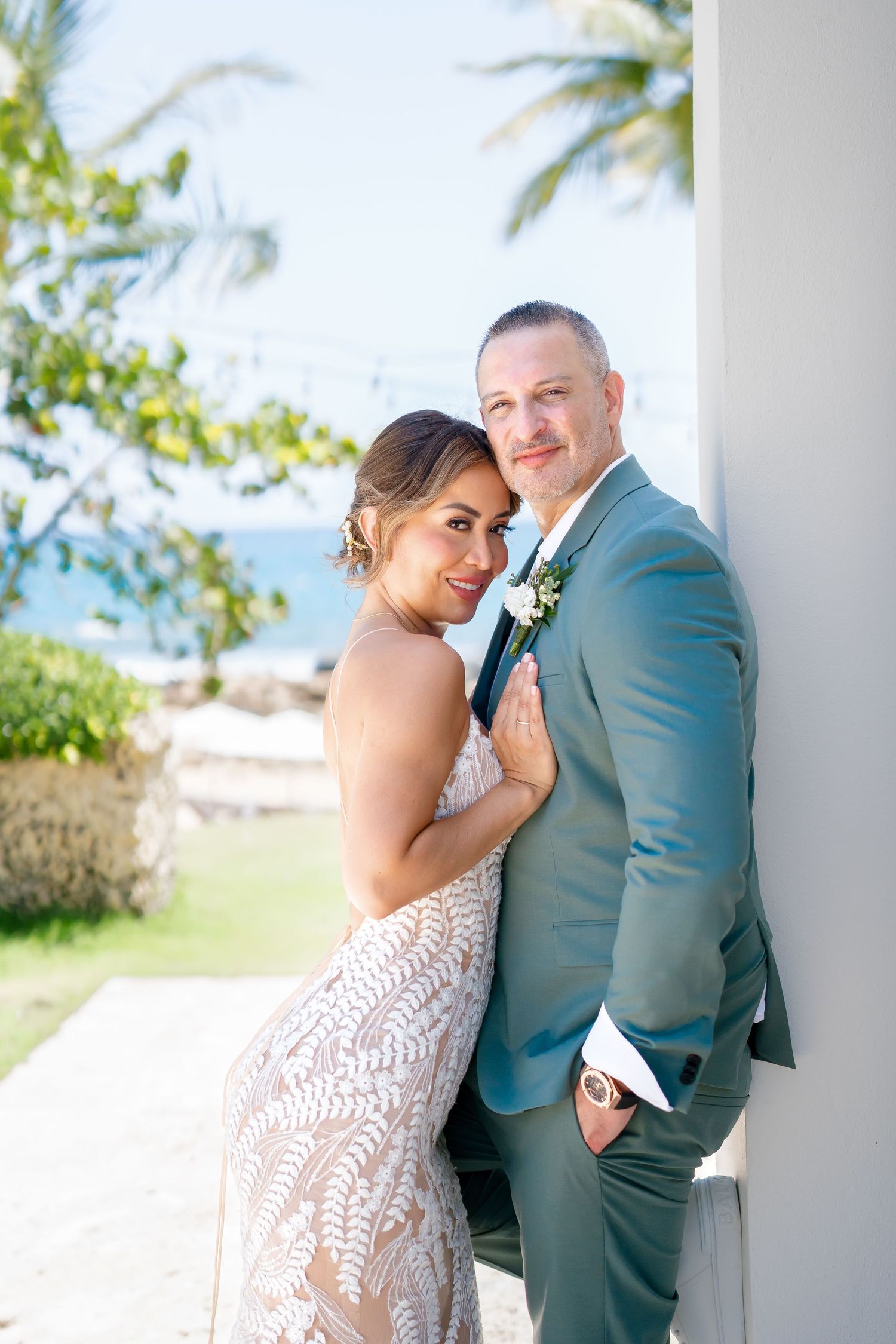 Romantic coastal wedding photos showing couple embracing against white pillars with ocean view.