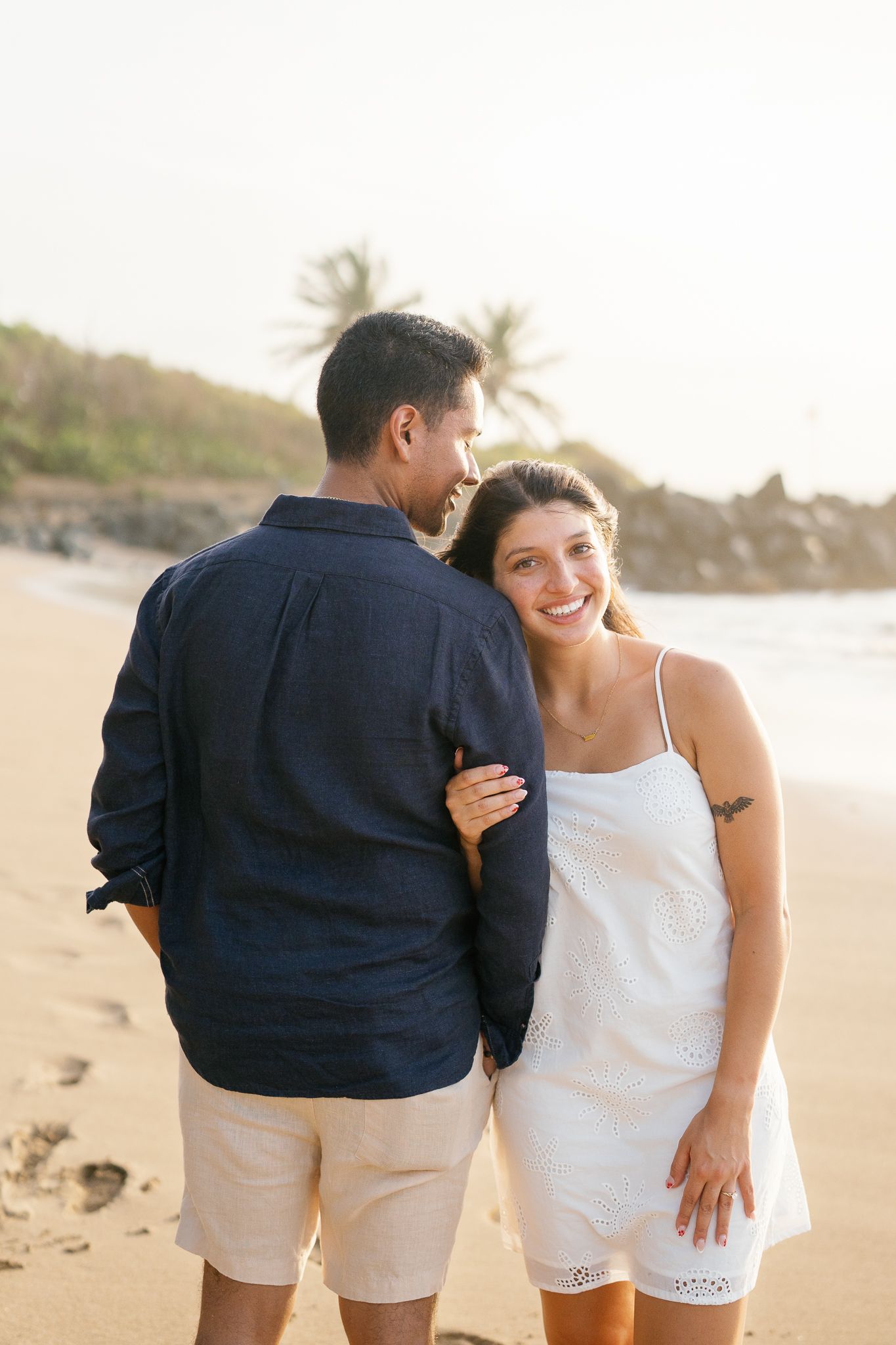 Romantic beach photoshoot showing playful moments between a couple in matching casual attire.