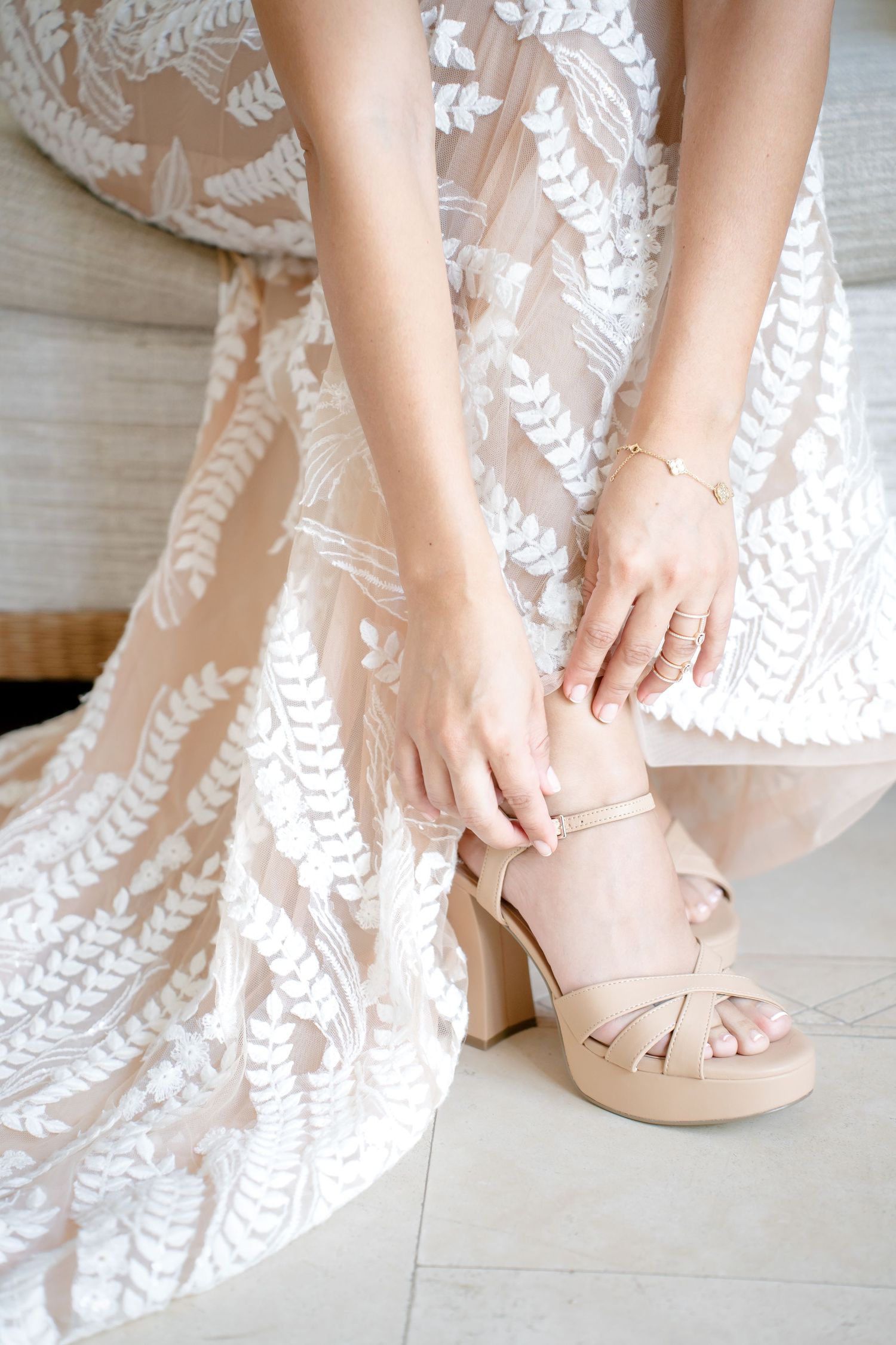 Close-up of nude colored wedding shoes with delicate details being put on with a white lace dress.