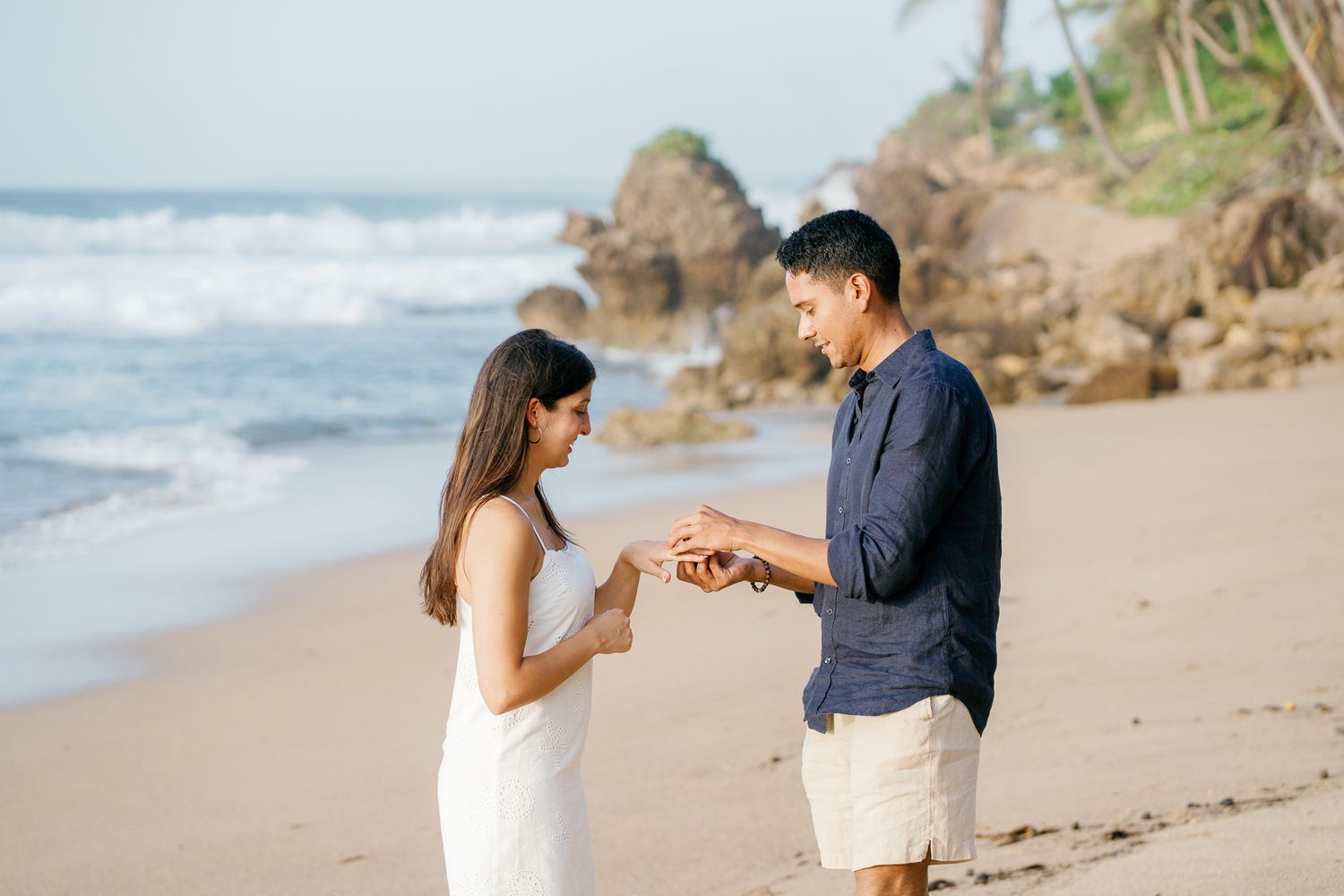 A romantic proposal scene unfolds on a scenic beach with crashing waves and rocky cliffs in the background.