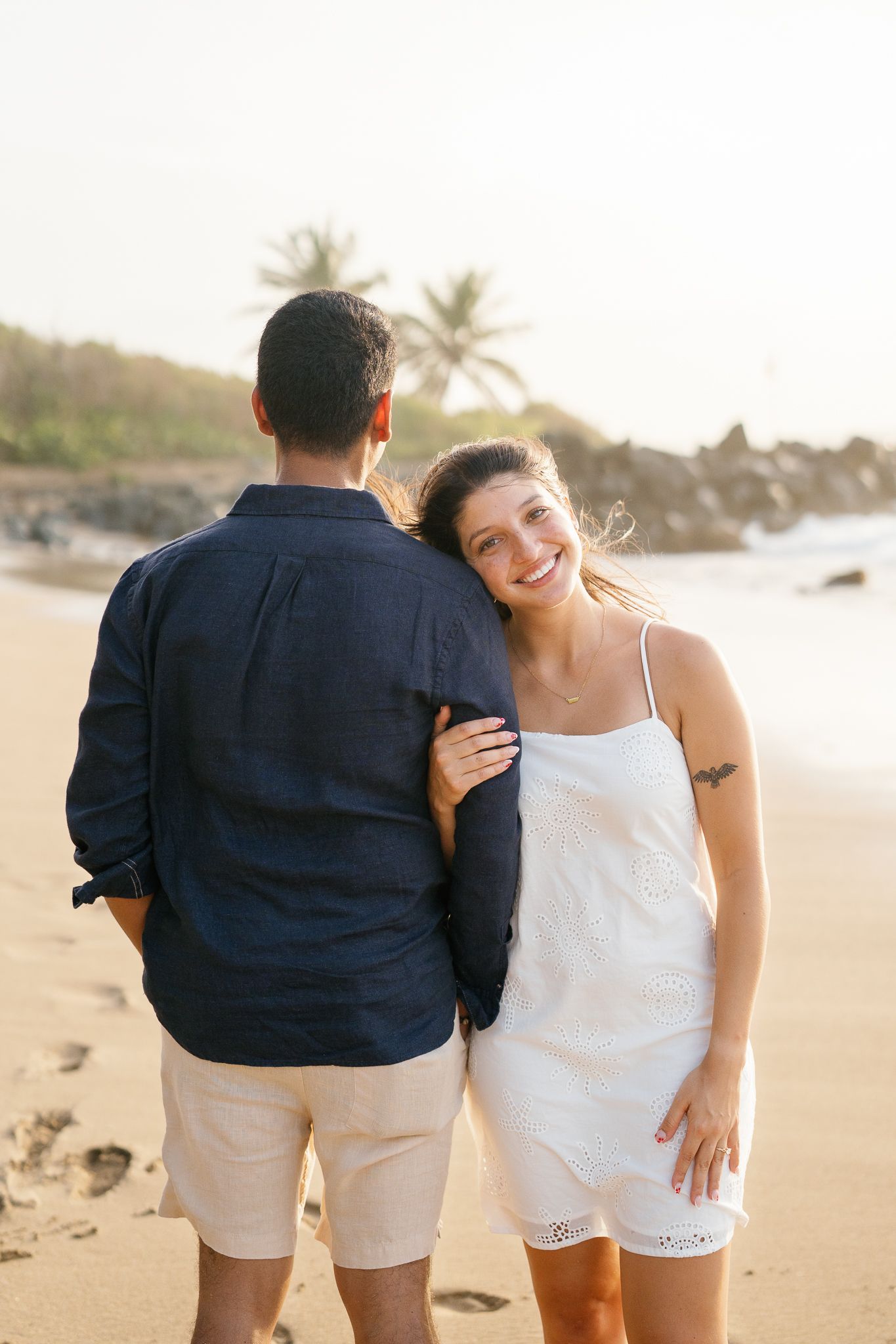 Couple walking together on a sandy beach at sunset wearing coordinated white and navy outfits.
