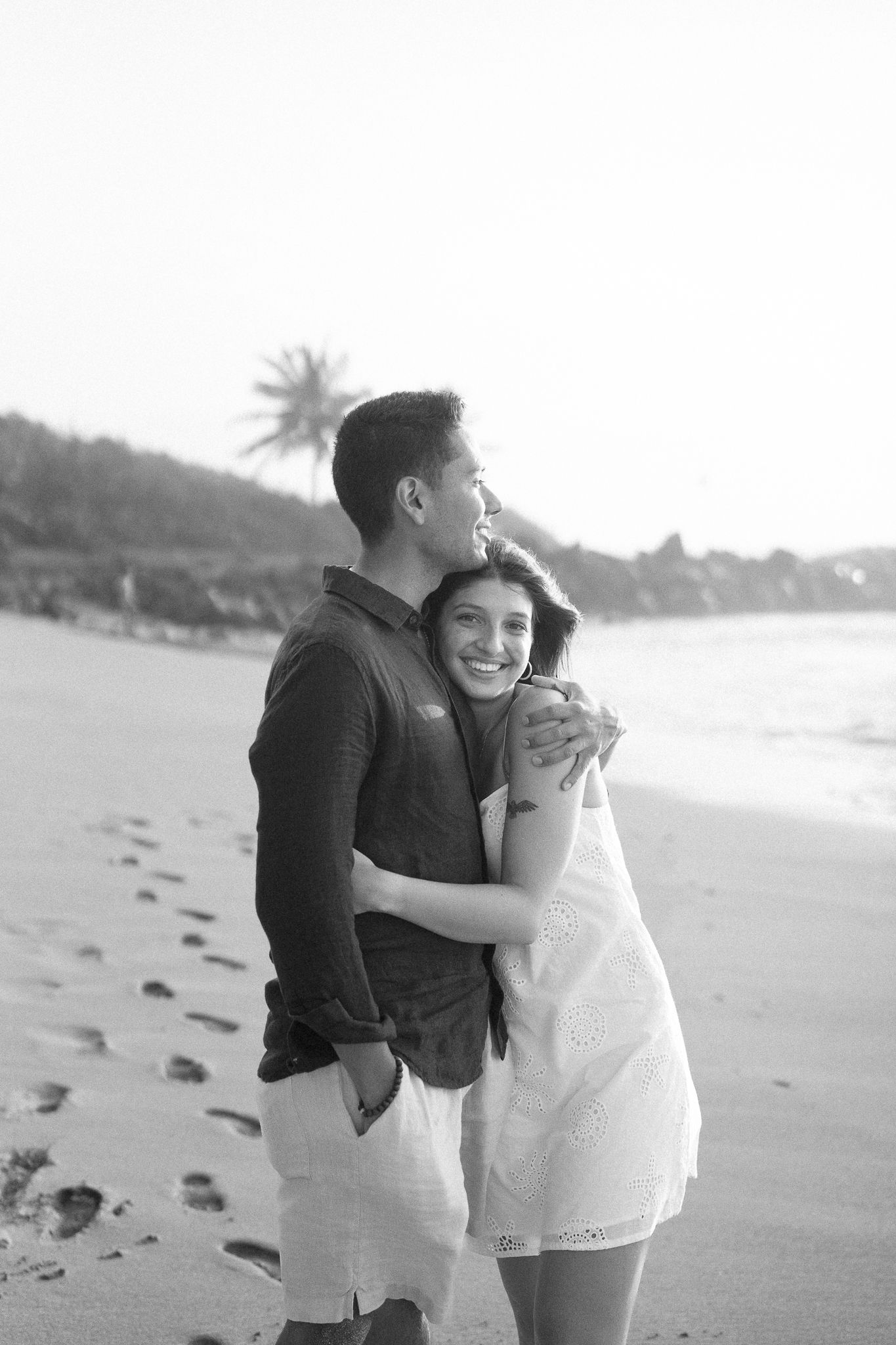 A couple laughs and hugs together during their black and white beach photoshoot.