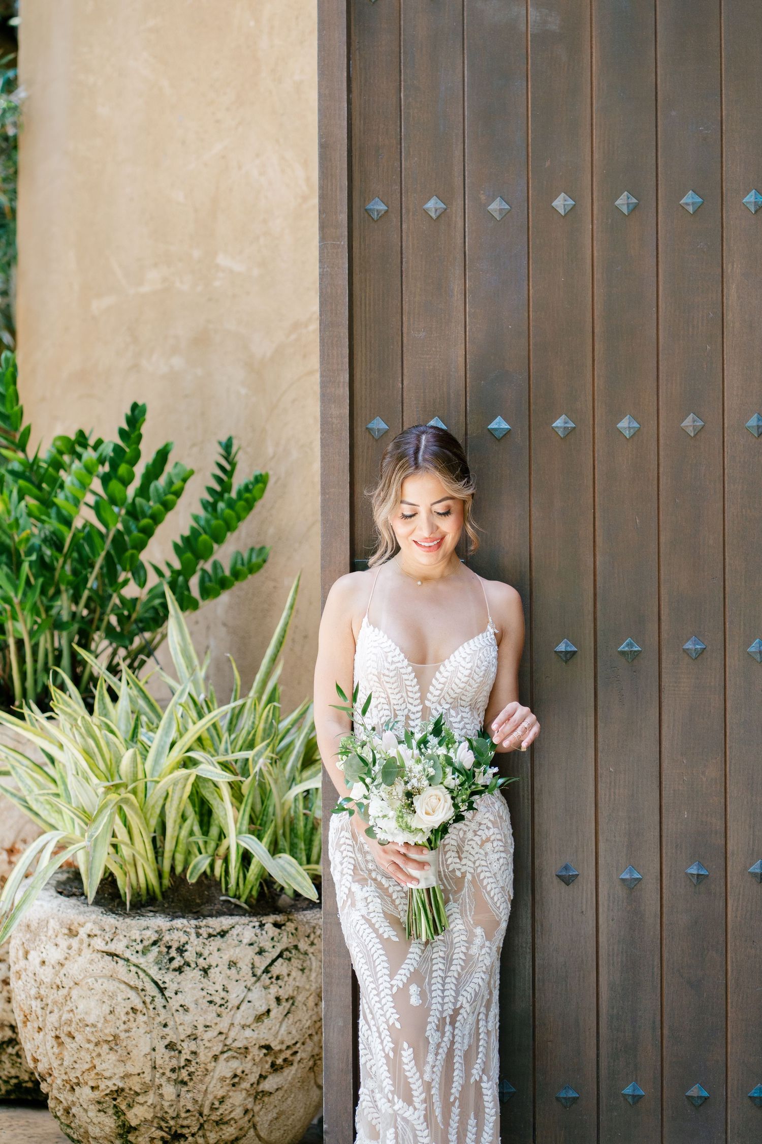 Elegant bridal portrait against wooden door with bouquet of white flowers.
