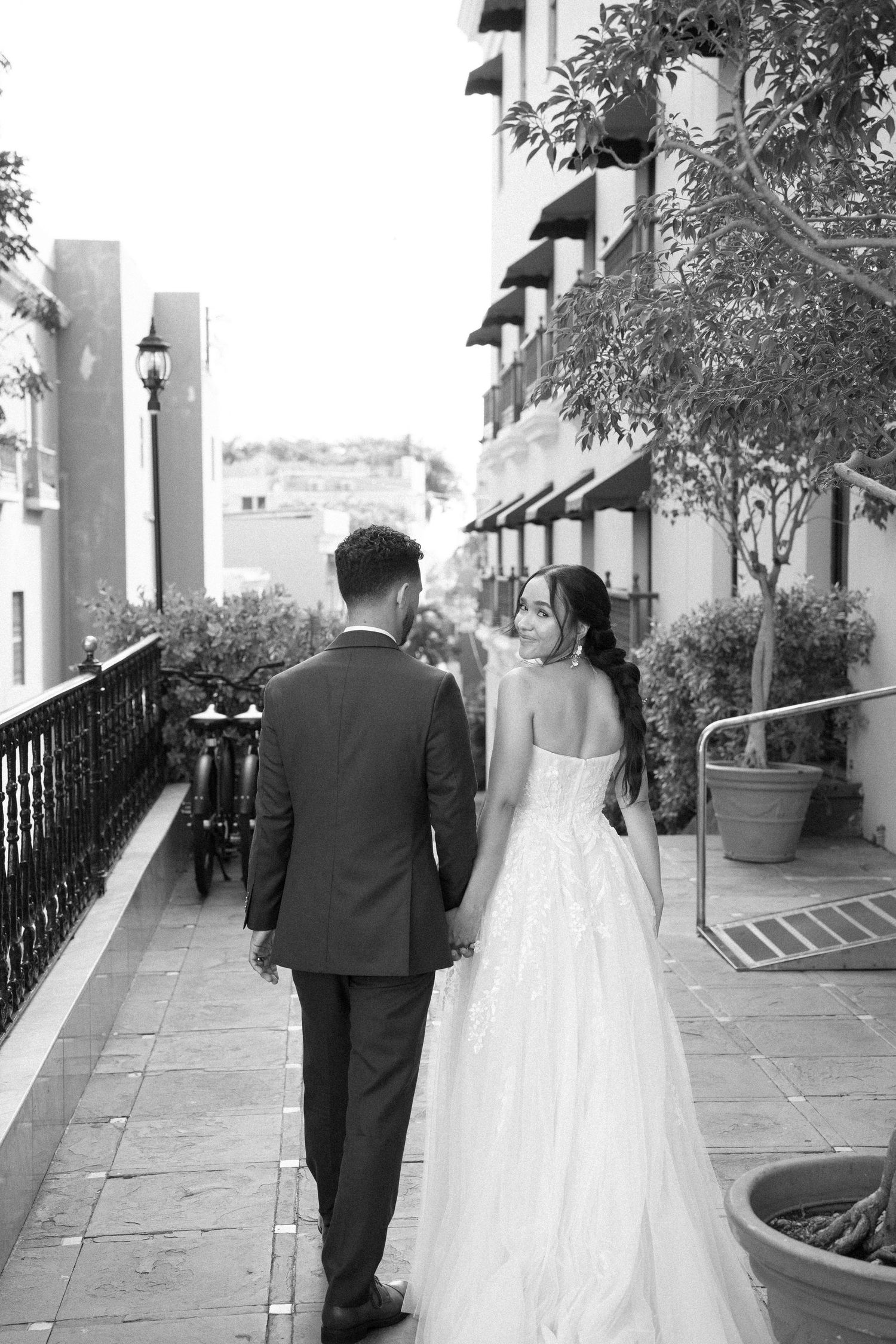 Black and white photo of a bride and groom walking hand in hand along a hotel corridor on their wedding day.