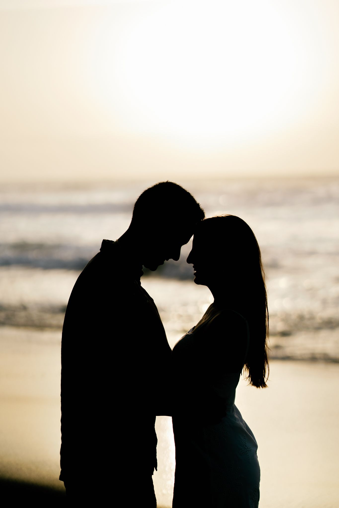Silhouetted couple in romantic embrace against sunset beach background creating dramatic backlit effect.