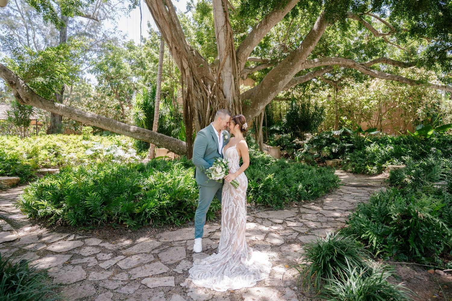 A couple walks along a stone path surrounded by lush green gardens at a romantic garden venue.
