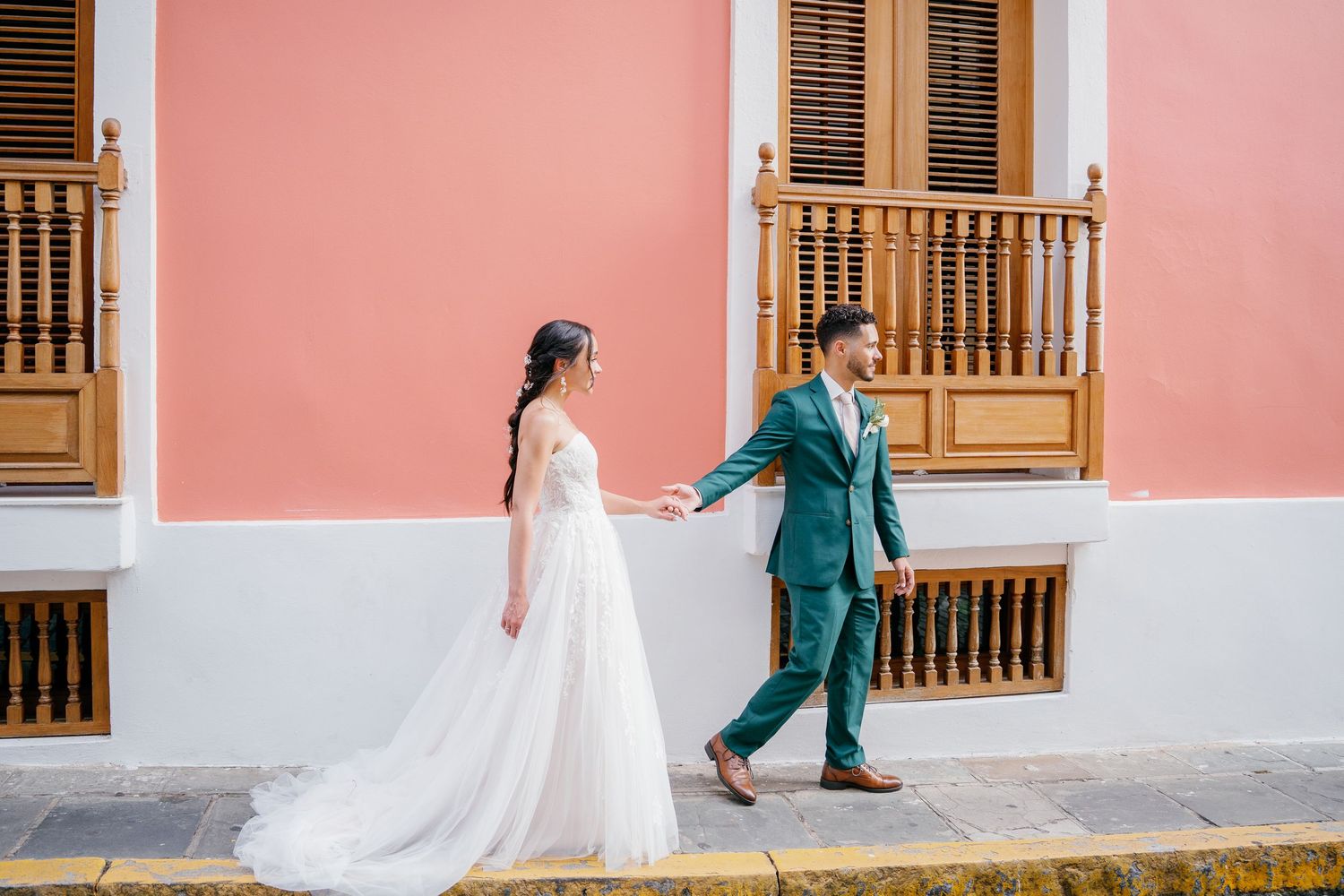 Bride and groom hold hands in front of a pink colonial building in Old San Juan, Puerto Rico.