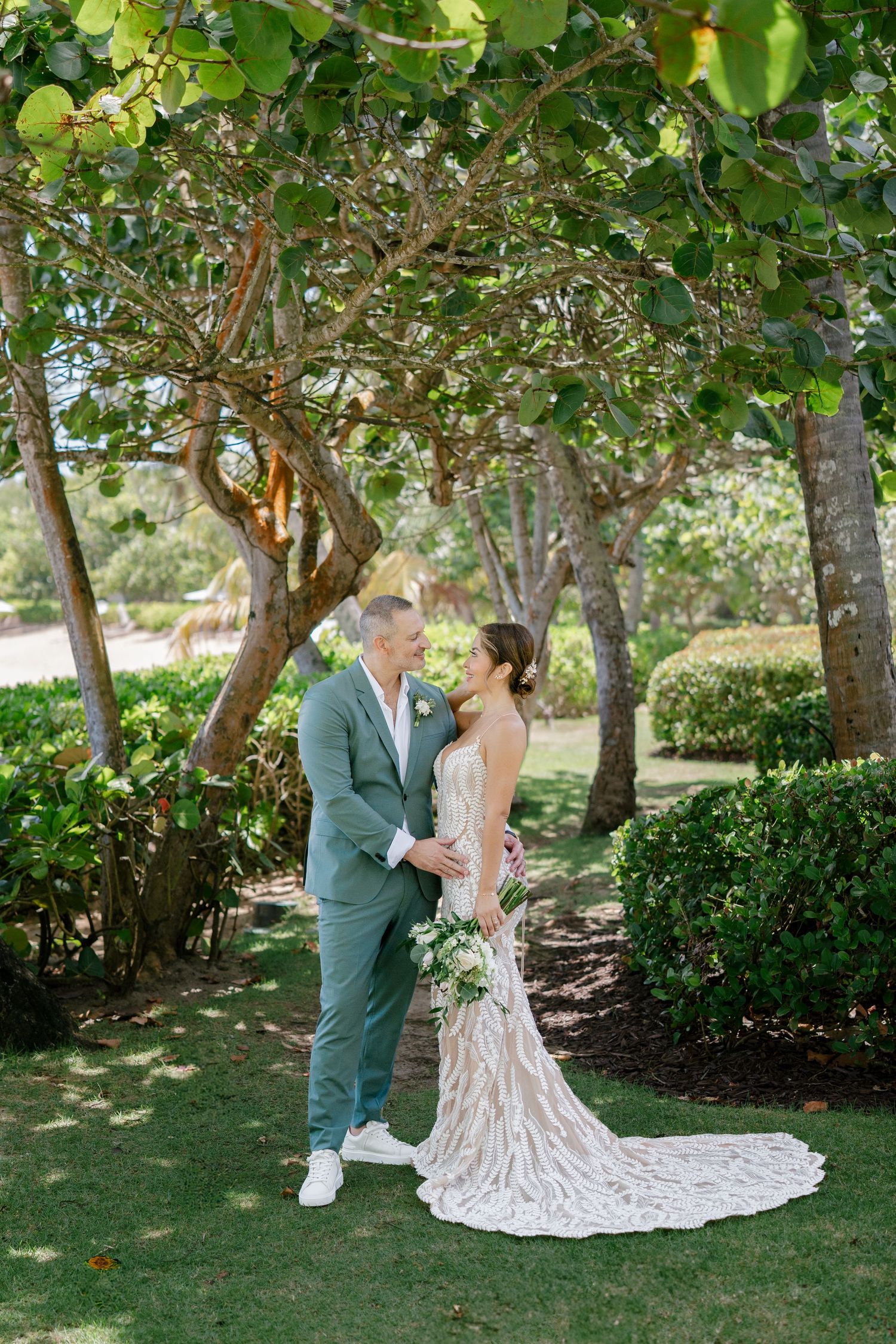 Wedding couple standing under trees in a garden with long train wedding dress.